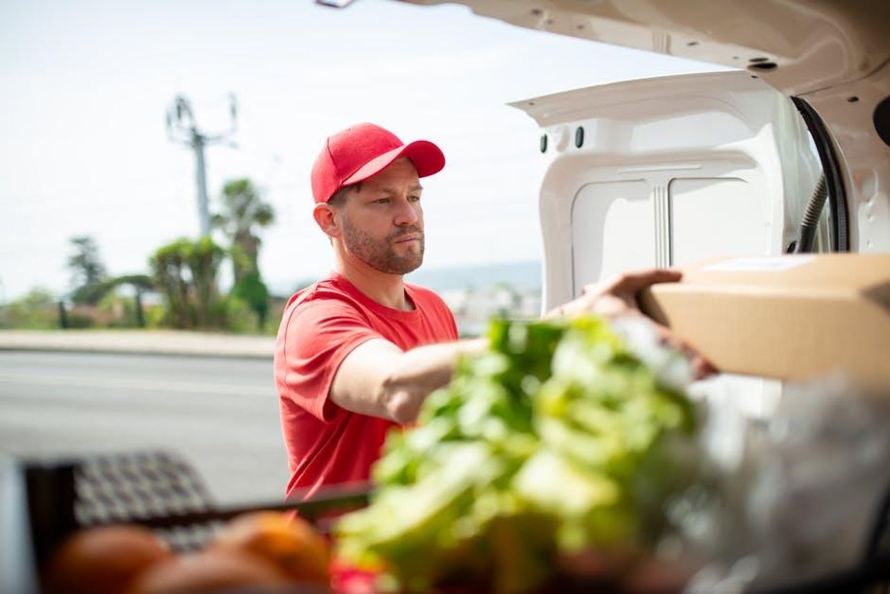 ACEA_e_il_futuro_della_forza_lavoro_automobilistica_DGyHeENCok - Veicoli24 Source: Kampus Production - pexels - A male delivery driver in a red uniform handling a parcel from a vehicle outdoors in Portugal.