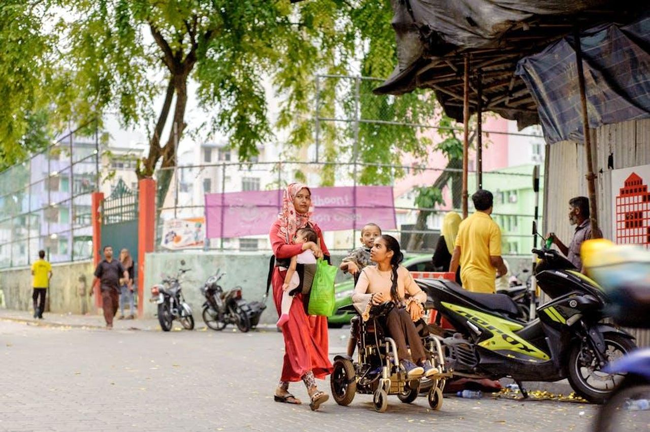 Accesso_limitato_per_i_motociclisti_nel_2025_KPLGT1Qf1L - Veicoli24 Source: Asad Photo Maldives - pexels - Two women, one in a wheelchair, navigate a lively urban street, capturing daily life and accessibility.