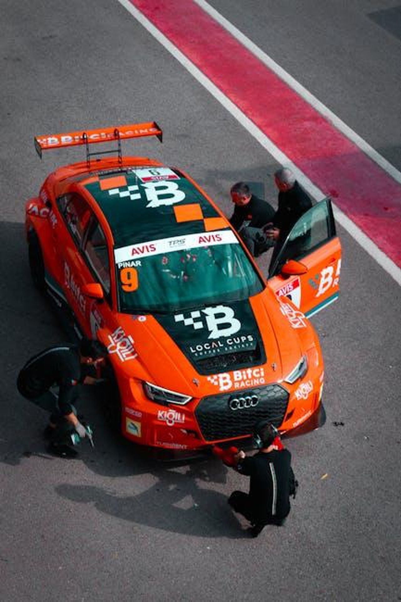 Audi_abbandona_la_strategia_di_denominazione_per_i_modelli_elettrici_vvOGOzInXb - Veicoli24 Source: Cuma Ersöz - pexels - Orange race car pit stop team at the track in Turkey, high angle view.