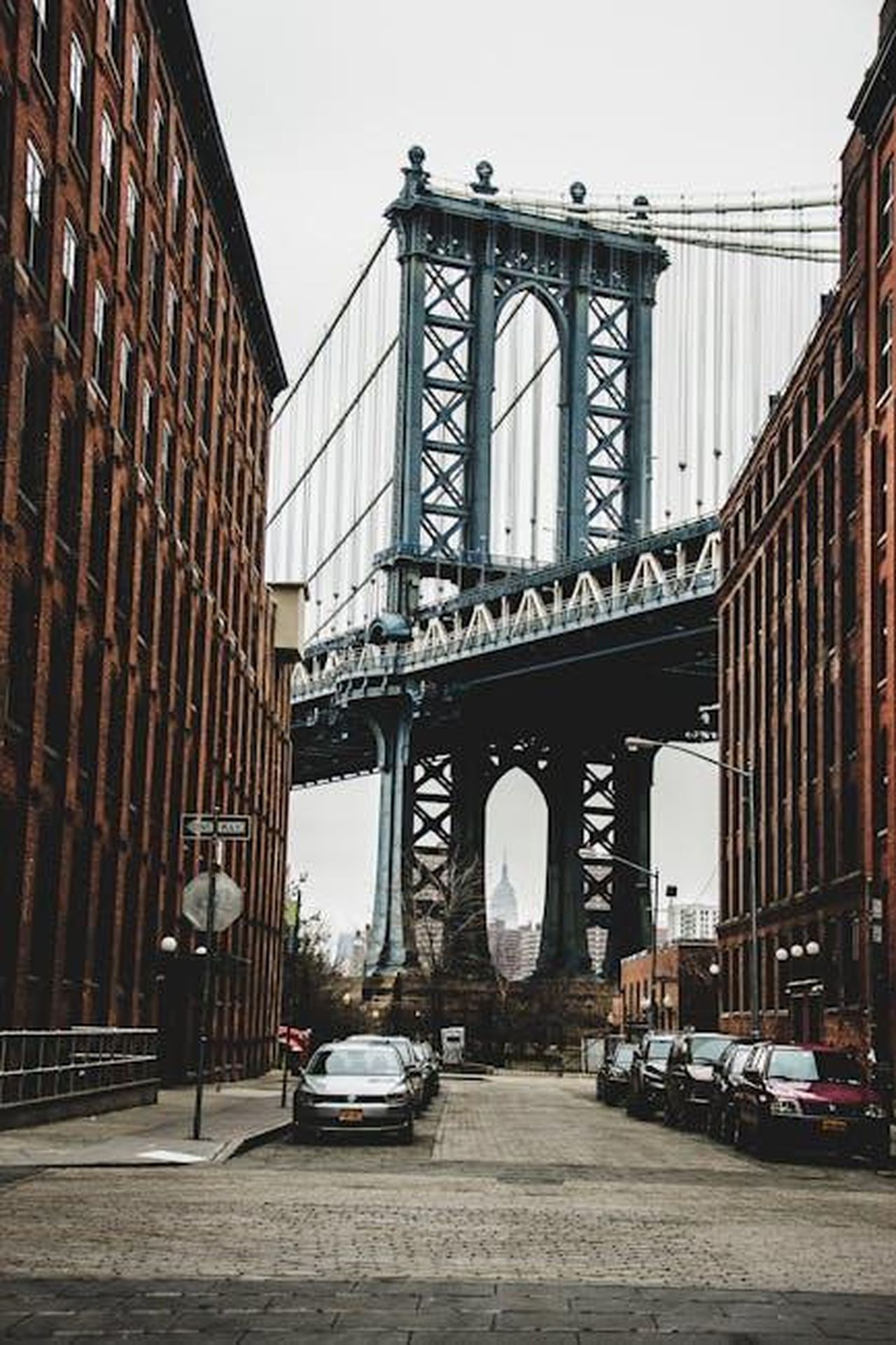 Aumento_della_provvista_per_risarcimenti_di_finanziamento_auto_UkolDHE1cq - Veicoli24 Source: Helena Lopes - pexels - View of Manhattan Bridge between red brick buildings, with cars parked on the street.