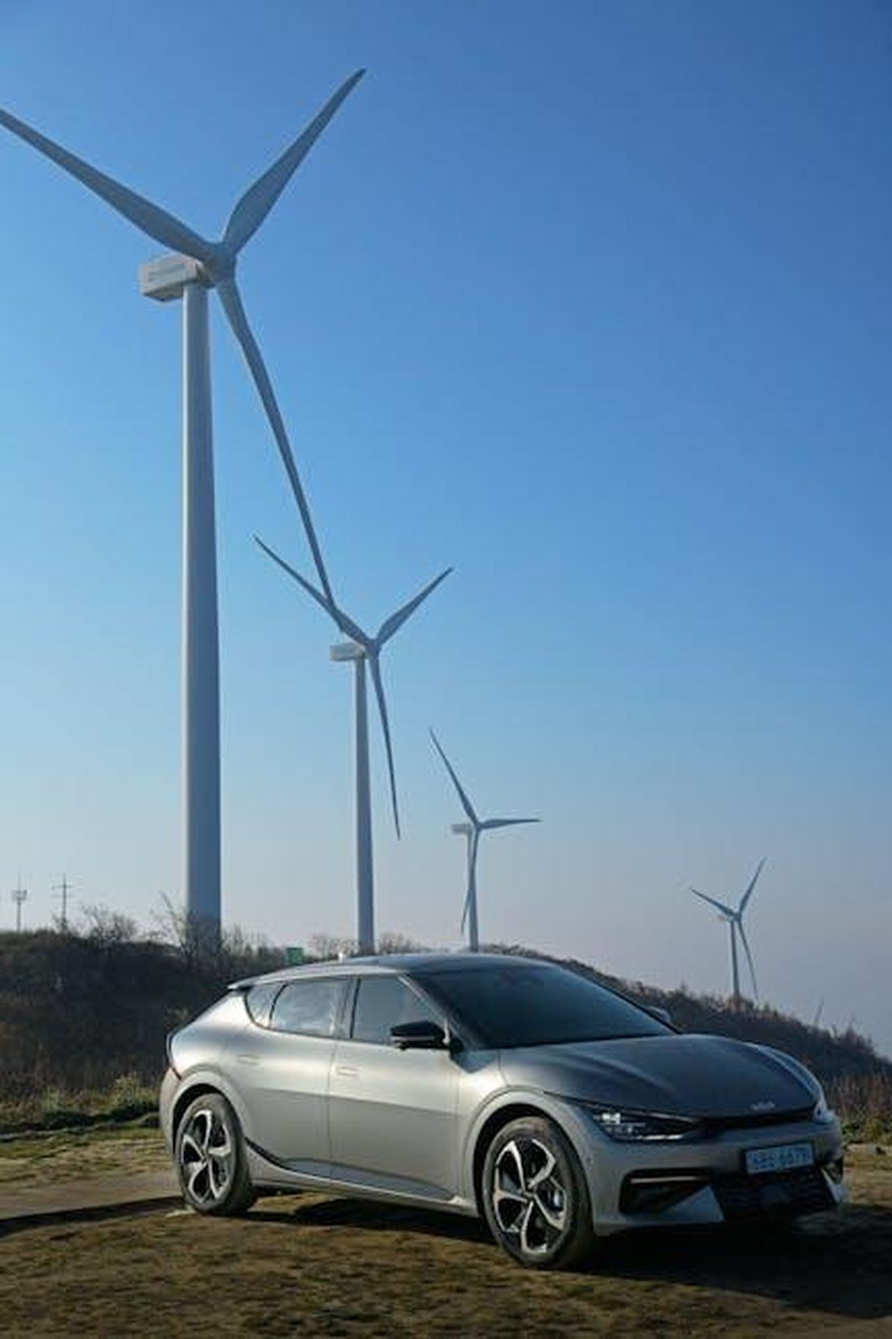Autonomia_e_tempi_di_ricarica_n10sKOVut7 - Veicoli24 Source: Hyundai Motor Group - pexels - Modern electric car parked near wind turbines under a clear blue sky.