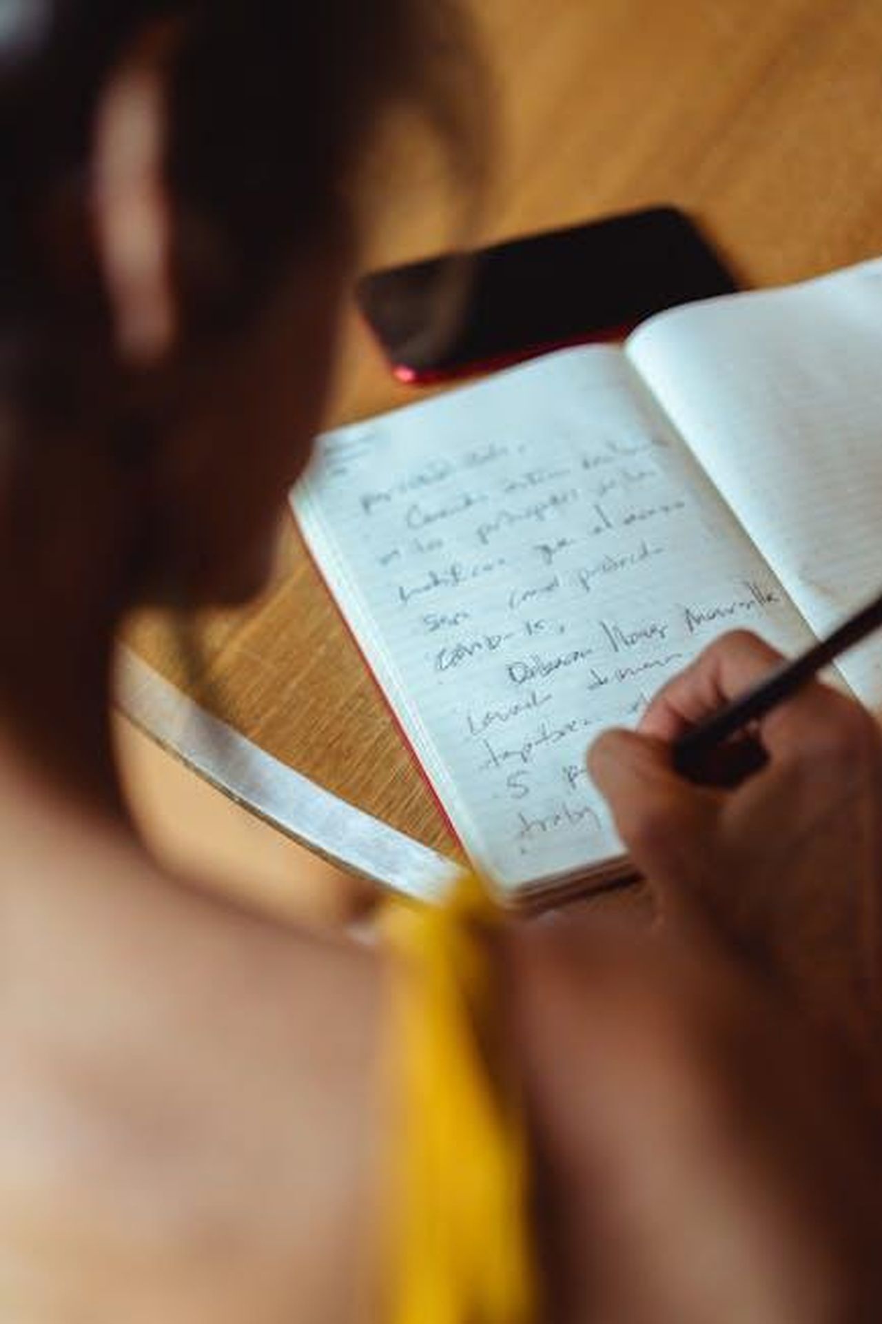 Autore_dellarticolo_GPxJ7EBEZE - Veicoli24 Source: Los Muertos Crew - pexels - A focused scene of someone writing in a notebook, accompanied by a smartphone placed on the table.