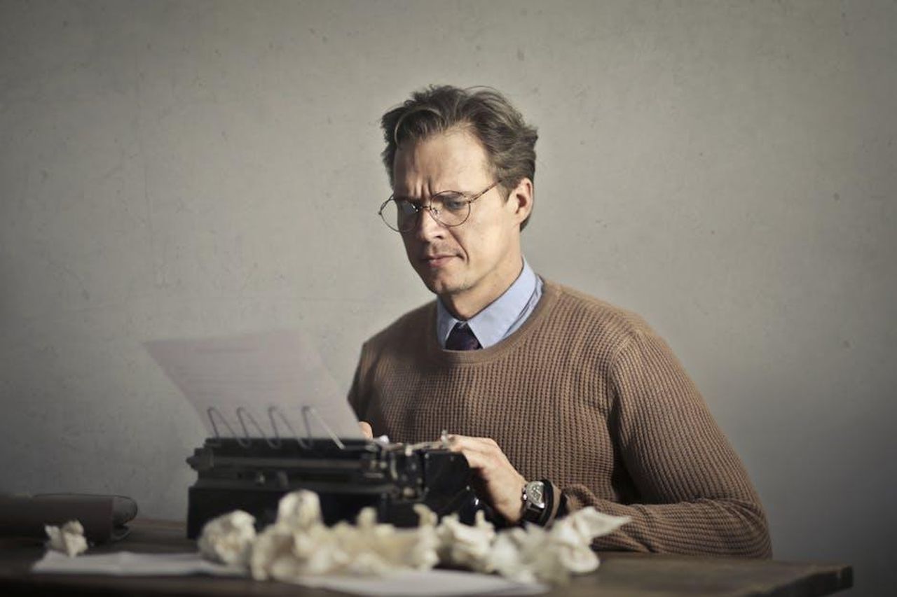 Autore_f9MGwiy2hy - Veicoli24 Source: Andrea Piacquadio - pexels - A thoughtful writer using a typewriter surrounded by crumpled paper, embodying vintage creativity.