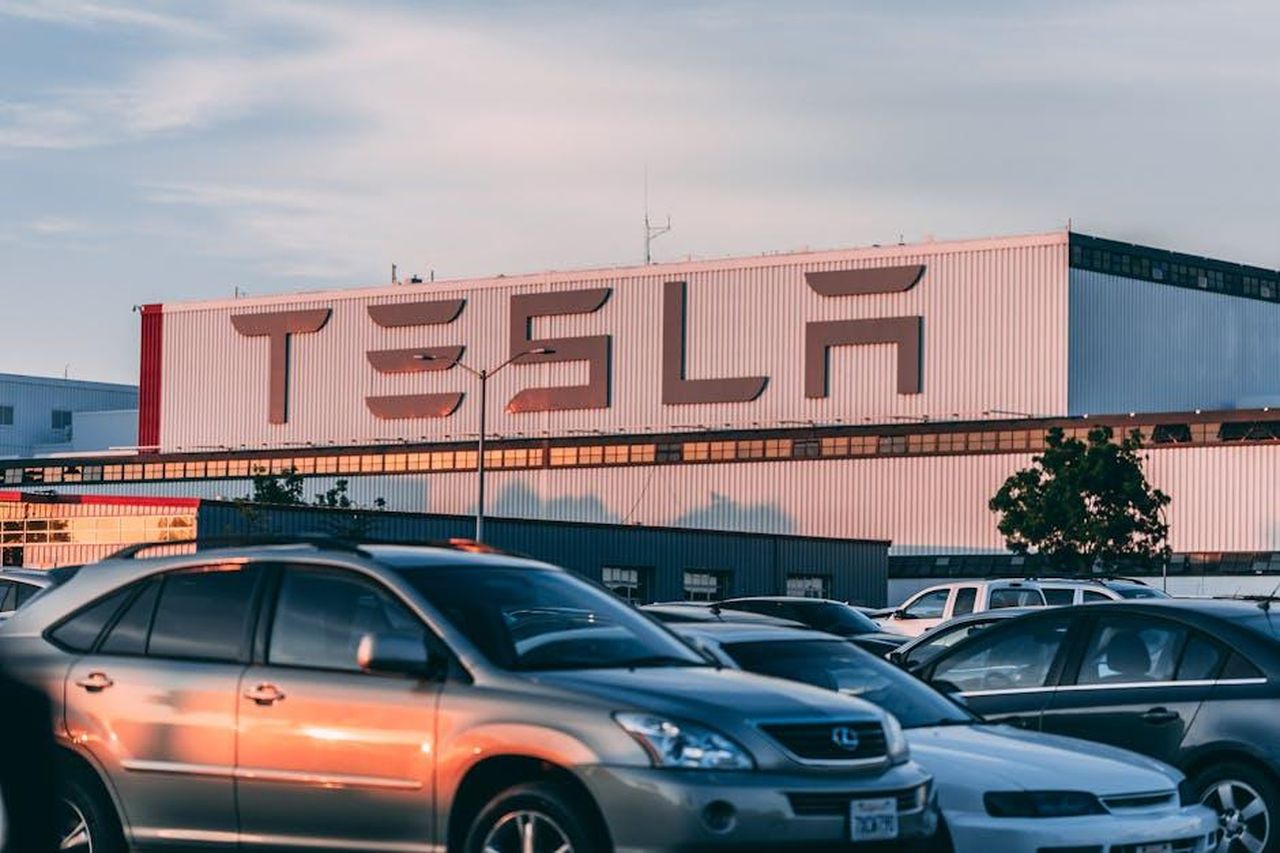 BYD_leader_del_mercato_globale_dei_veicoli_elettrici_WNWjgKHFLx - Veicoli24 Source: Craig Adderley - pexels - Tesla factory with parked cars during sunset, showcasing modern automotive industry vibes.