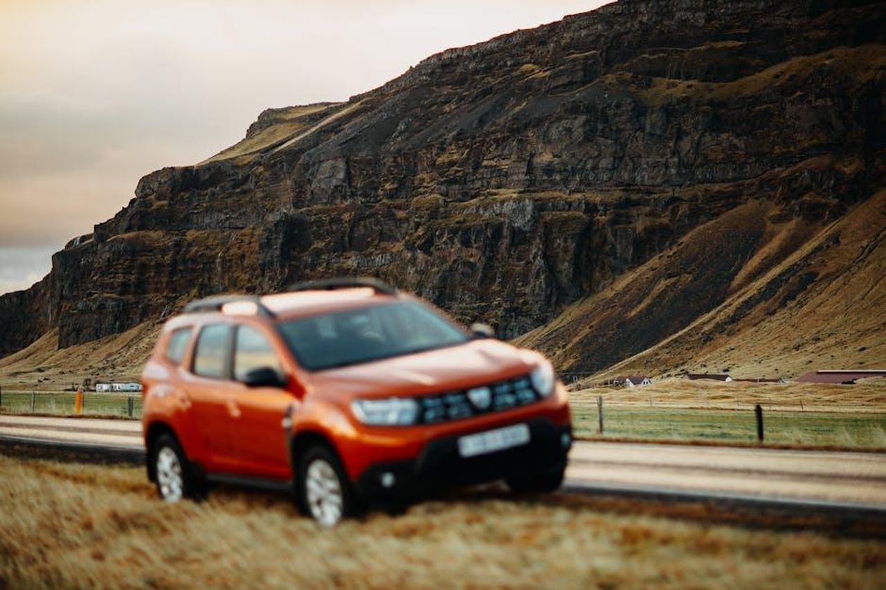 Caratteristiche_XglQpCVlLF - Veicoli24 Source: Matheus Bertelli - pexels - An orange SUV parked on a rural road beside a rugged hillside, captured in a scenic outdoor setting.
