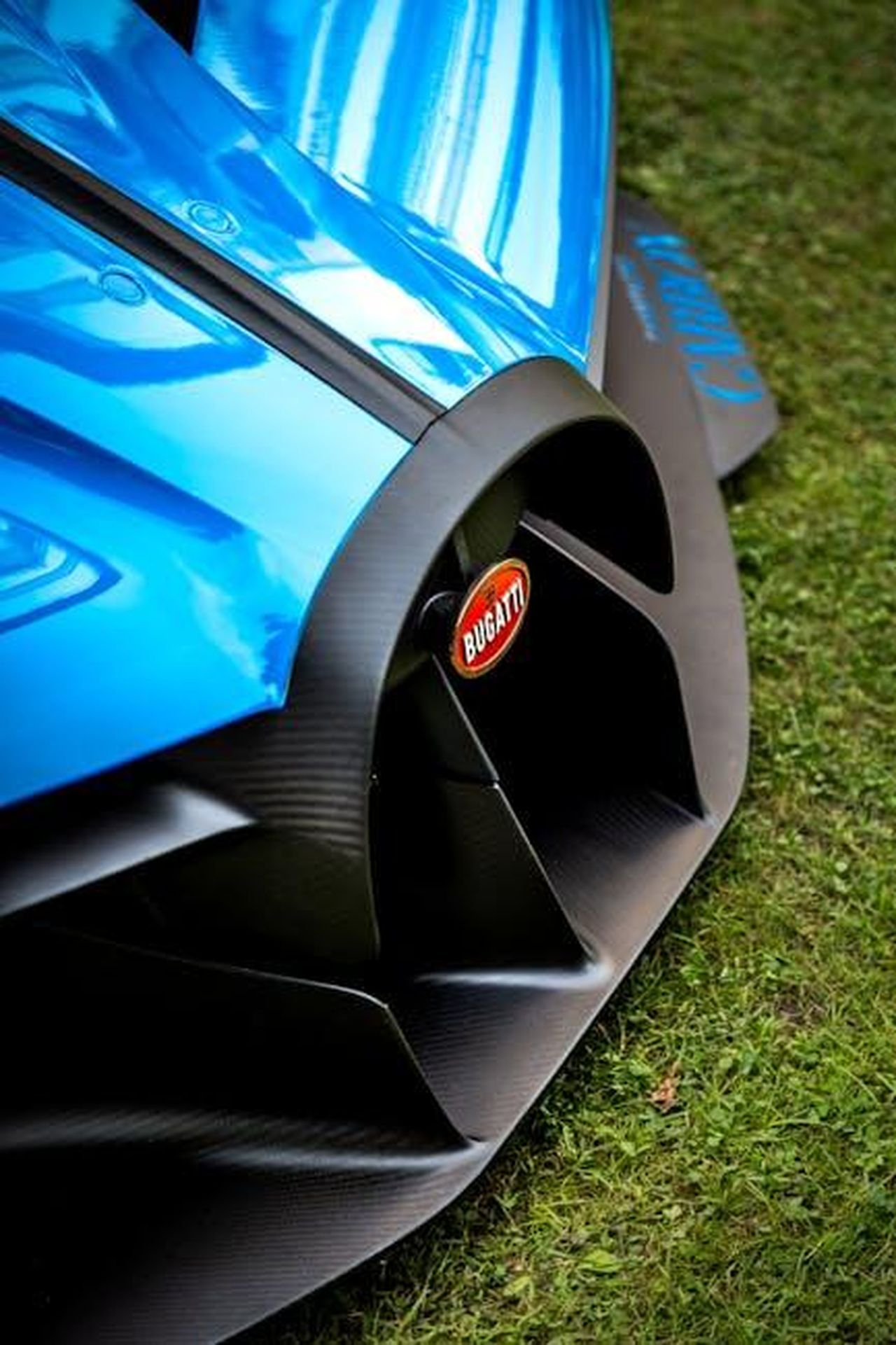 Caratteristiche_e_prestazioni_della_Bugatti_Mistral_WGXEOBrUrE - Veicoli24 Source: Quentin Martinez - pexels - Close-up of a blue Bugatti's front detail showcasing sleek design on grass.
