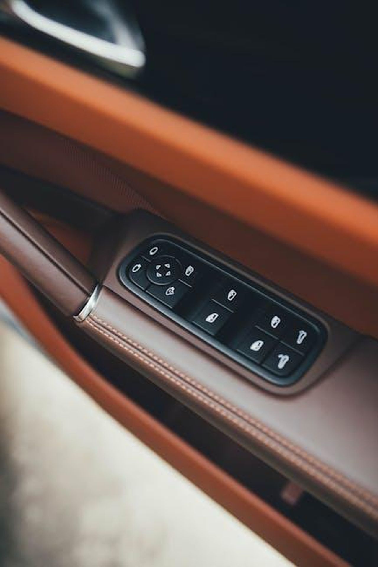 Caratteristiche_e_specifiche_IVcRTEWlUM - Veicoli24 Source: Mohit Hambiria - pexels - Close-up of a luxury car interior showing brown leather and control buttons on the door panel.