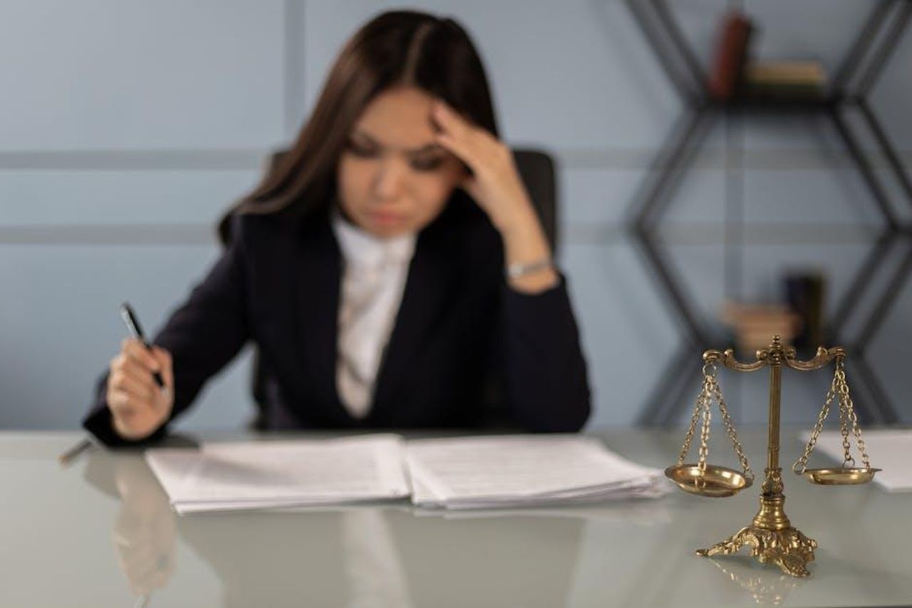Carriera_di_Reynolds_prima_di_Toyota_U0ALm9NLBR - Veicoli24 Source: KATRIN BOLOVTSOVA - pexels - A fatigued female lawyer reviewing documents with a justice scale nearby, emphasizing stress in legal work.