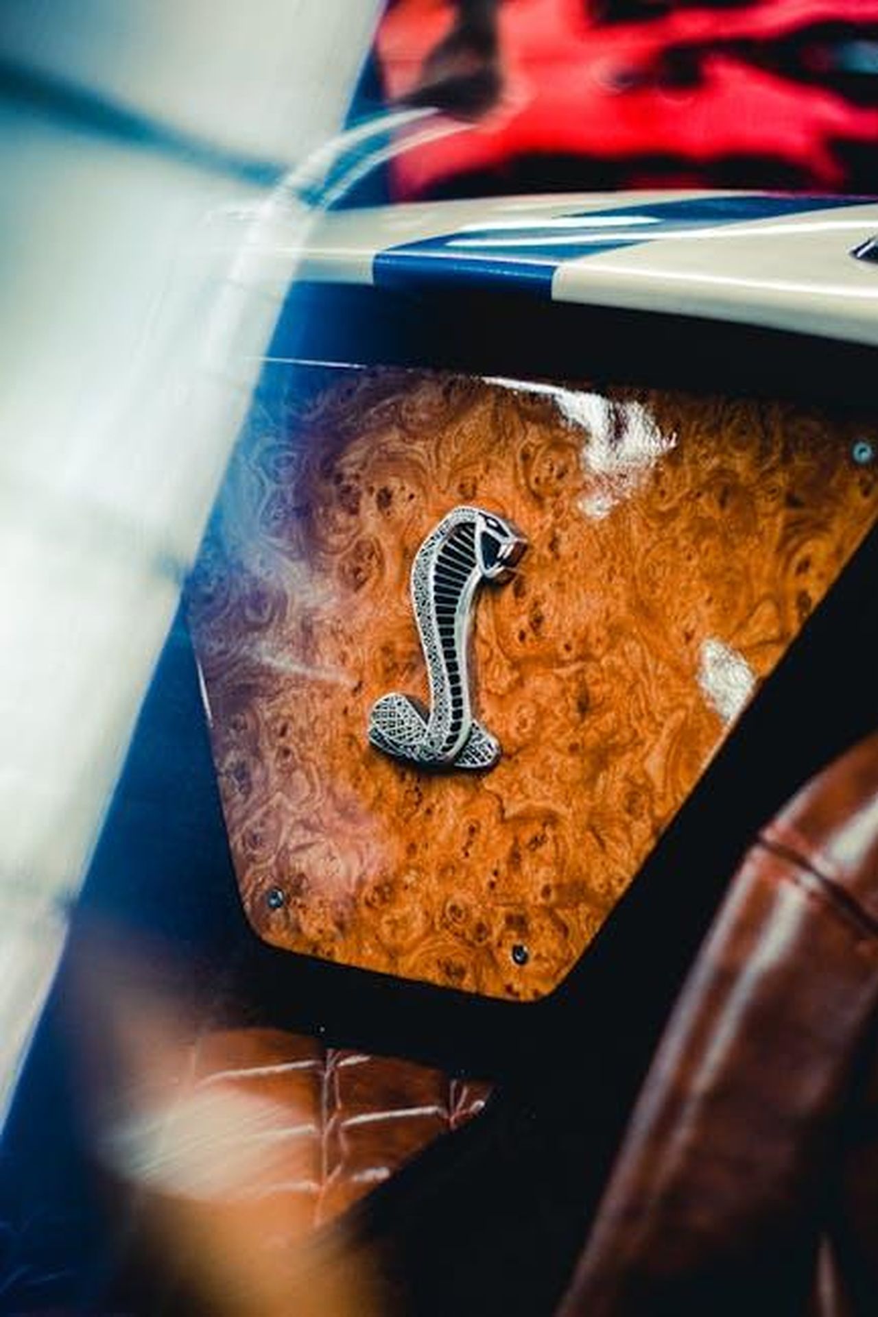 Cobra_GT_caratteristiche_e_opzioni_ue9OxPeMJF - Veicoli24 Source: Mario Alvarado - pexels - Close-up of a vintage car interior showcasing a Shelby Cobra emblem on a wooden dashboard.