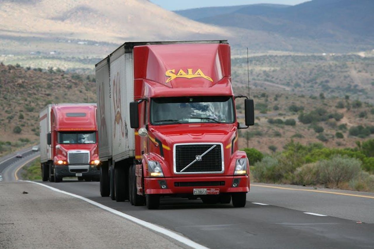 Come_Volvo_sta_gestendo_il_richiamo_kaKzHK8ERs - Veicoli24 Source: CARLOSCRUZ ARTEGRAFIA - pexels - Red trucks driving through a scenic desert landscape showcasing transportation logistics.