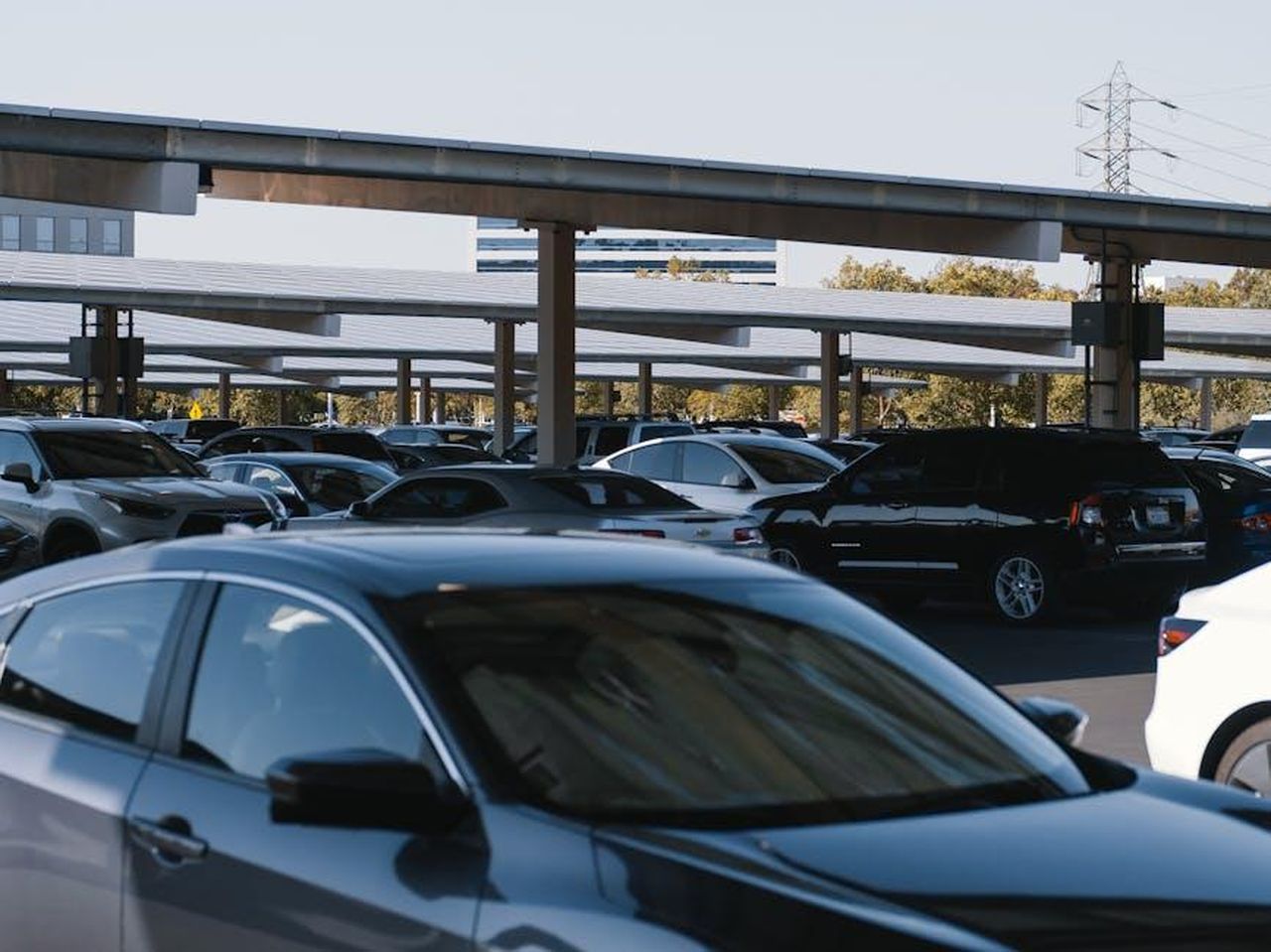 Competizione_nel_mercato_delle_auto_ibride_mHgmmQyM2J - Veicoli24 Source: Kindel Media - pexels - A busy outdoor parking lot filled with various parked cars under solar panel structures.