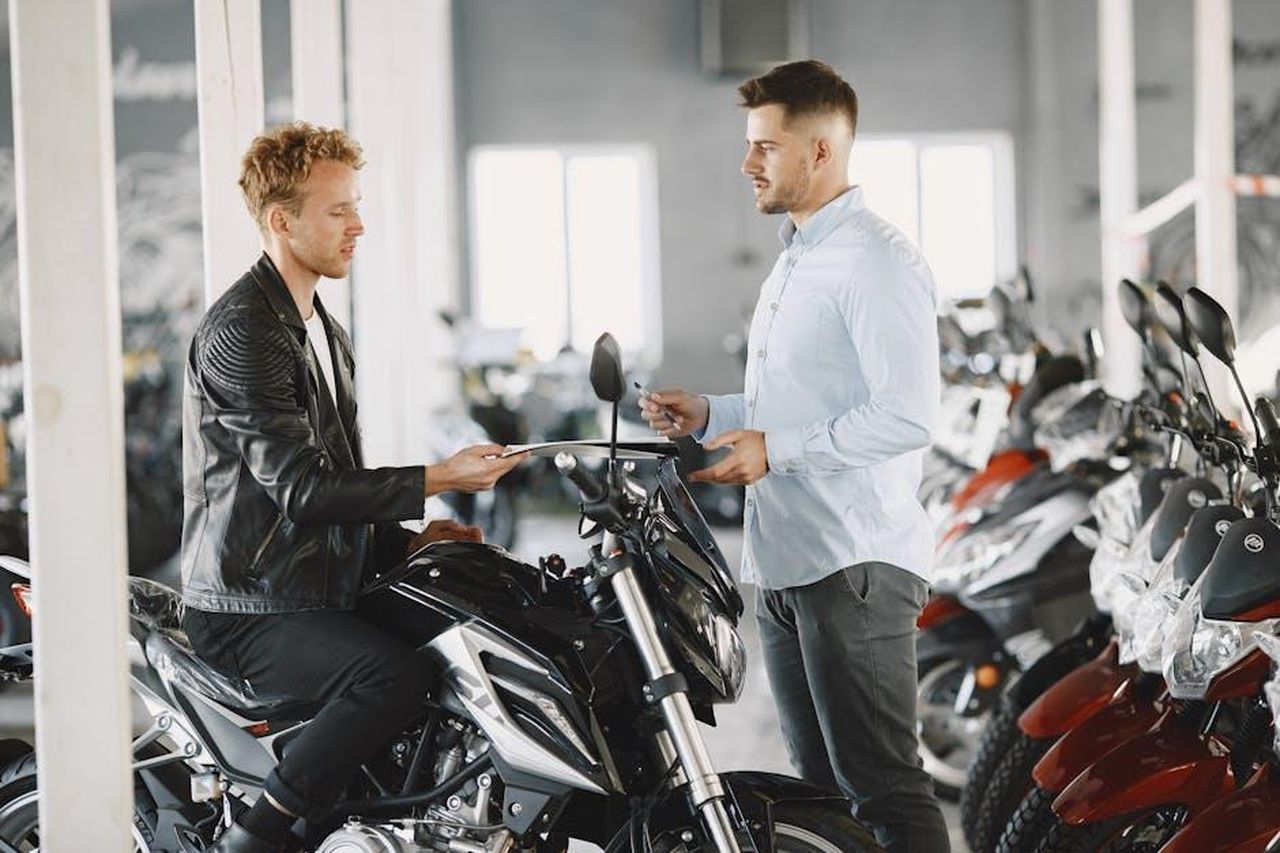 Consiglio_per_lacquisto_zMCe5Lbmbm - Veicoli24 Source: Gustavo Fring - pexels - Two men in a motorcycle dealership discussing a potential motorcycle purchase.