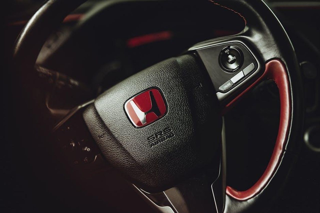 Cosa_ci_piace_della_Honda_Odyssey_2025_n7q0cel4Um - Veicoli24 Source: Jay Johnson - pexels - Detailed view of a sleek car's steering wheel showcasing the distinct red logo emblem.