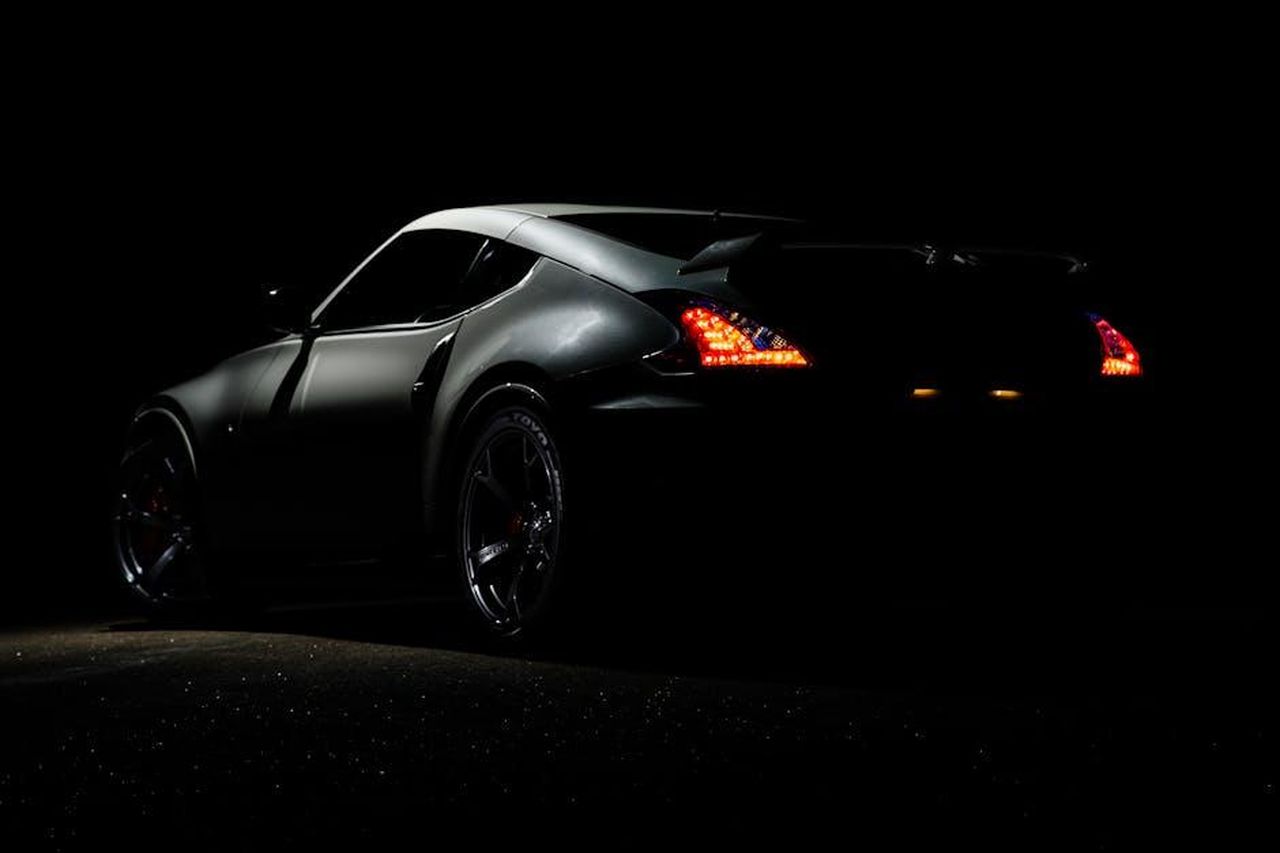 Cosa_ci_piace_sENIUtxUAI - Veicoli24 Source: Albin Berlin - pexels - A dramatic shot of a Nissan 370Z sports car illuminated in darkness with vibrant tail lights.