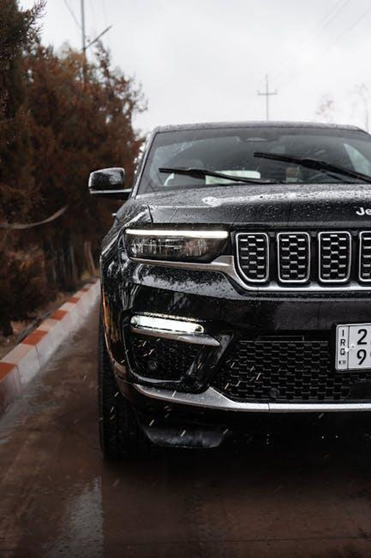Cosa_sono_gli_pneumatici_allweather_8ZCJ2Bbwb6 - Veicoli24 Source: 04iraq - pexels - Close-up of a Jeep Grand Cherokee parked on a rainy road with reflections and wet surface details.
