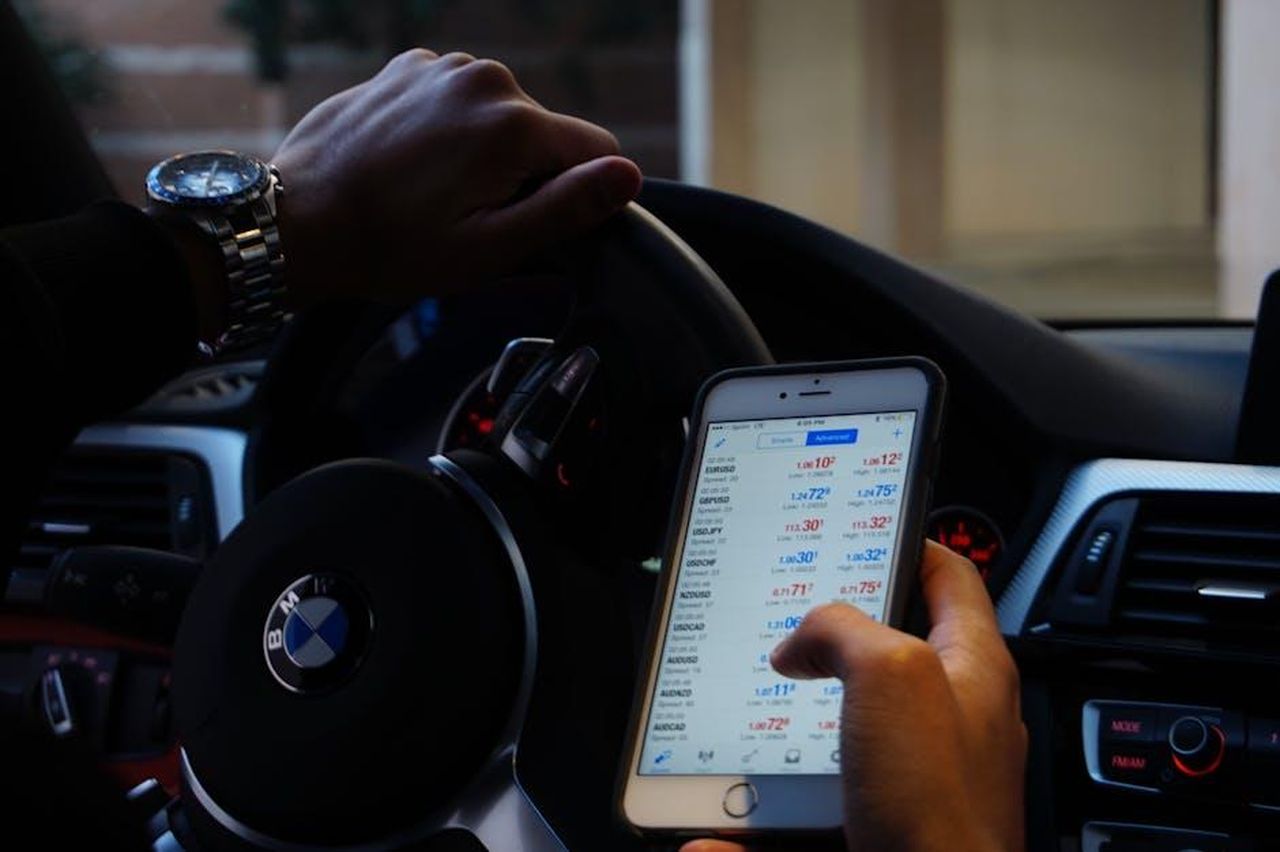 Dati_sul_mercato_della_finanza_auto_usata_mLPN0Oh3OO - Veicoli24 Source: D'Vaughn Bell - pexels - Person using mobile phone for currency trading while driving BMW car.