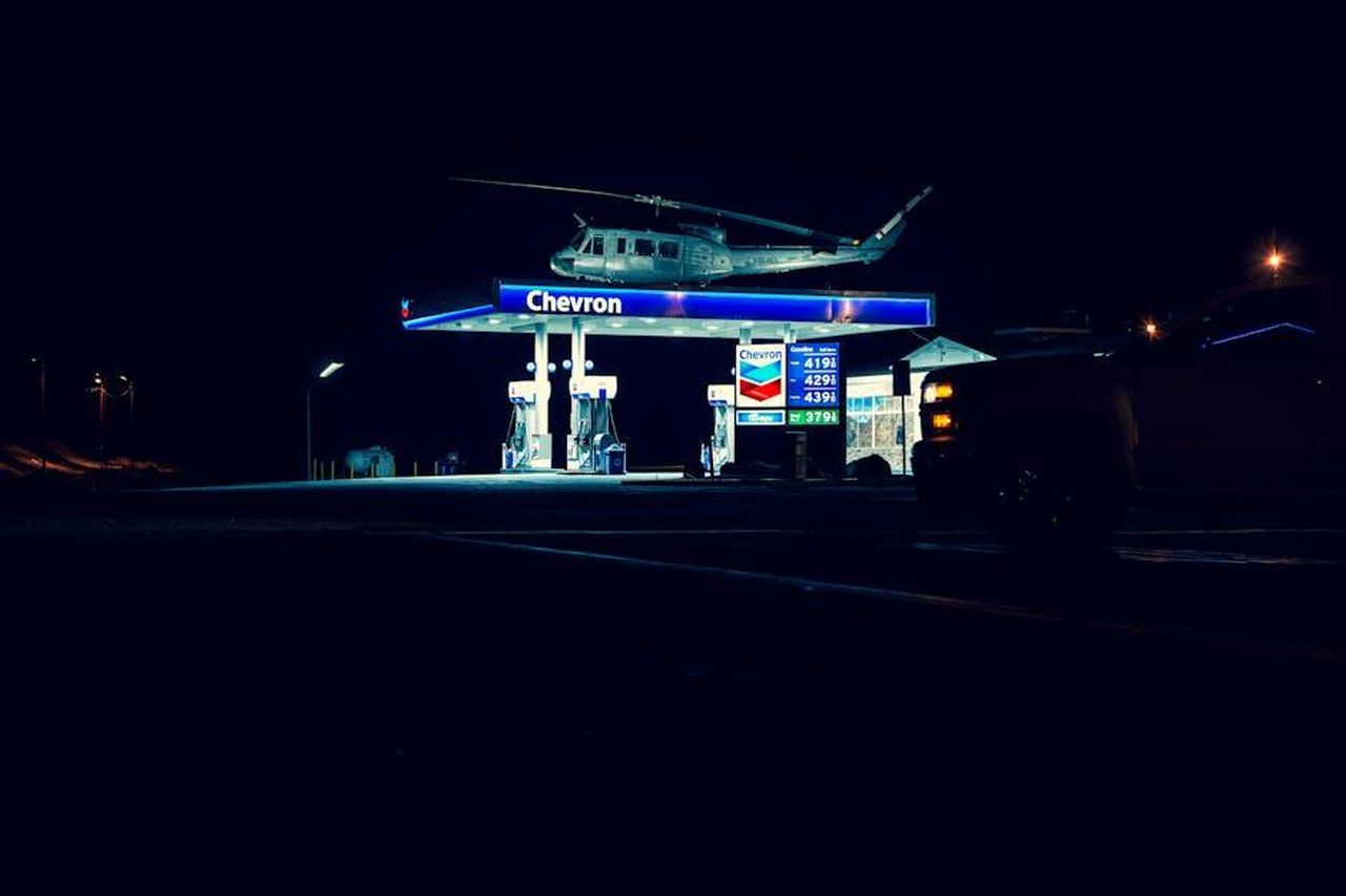 Declino_dei_veicoli_a_diesel_e_benzina_xu4OcK68sr - Veicoli24 Source: Derwin Edwards - pexels - A helicopter hovering above a lit Chevron gas station during nighttime, creating a unique urban scene.