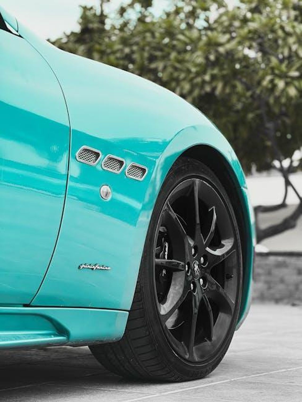 Design_e_comfort_del_nuovo_GranCabrio_E3qPcYxMVD - Veicoli24 Source: Ali Babajahdi - pexels - Detailed shot of a turquoise Maserati car wheel, emphasizing design and style.