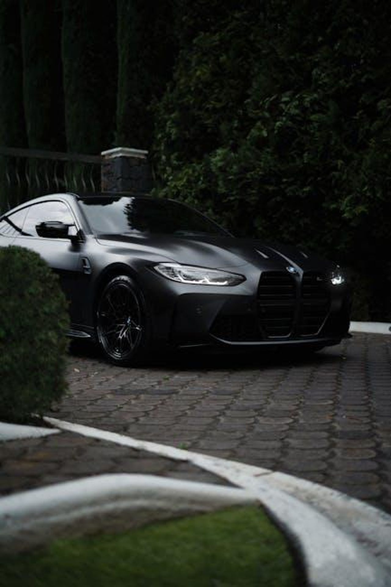 Dettagli_e_caratteristiche_della_M4_CS_Edition_VR46_8aRWkeTzu7 - Veicoli24 Source: Alan Cordero - pexels - A sleek black BMW M4 parked elegantly on a cobblestone driveway, surrounded by lush greenery.