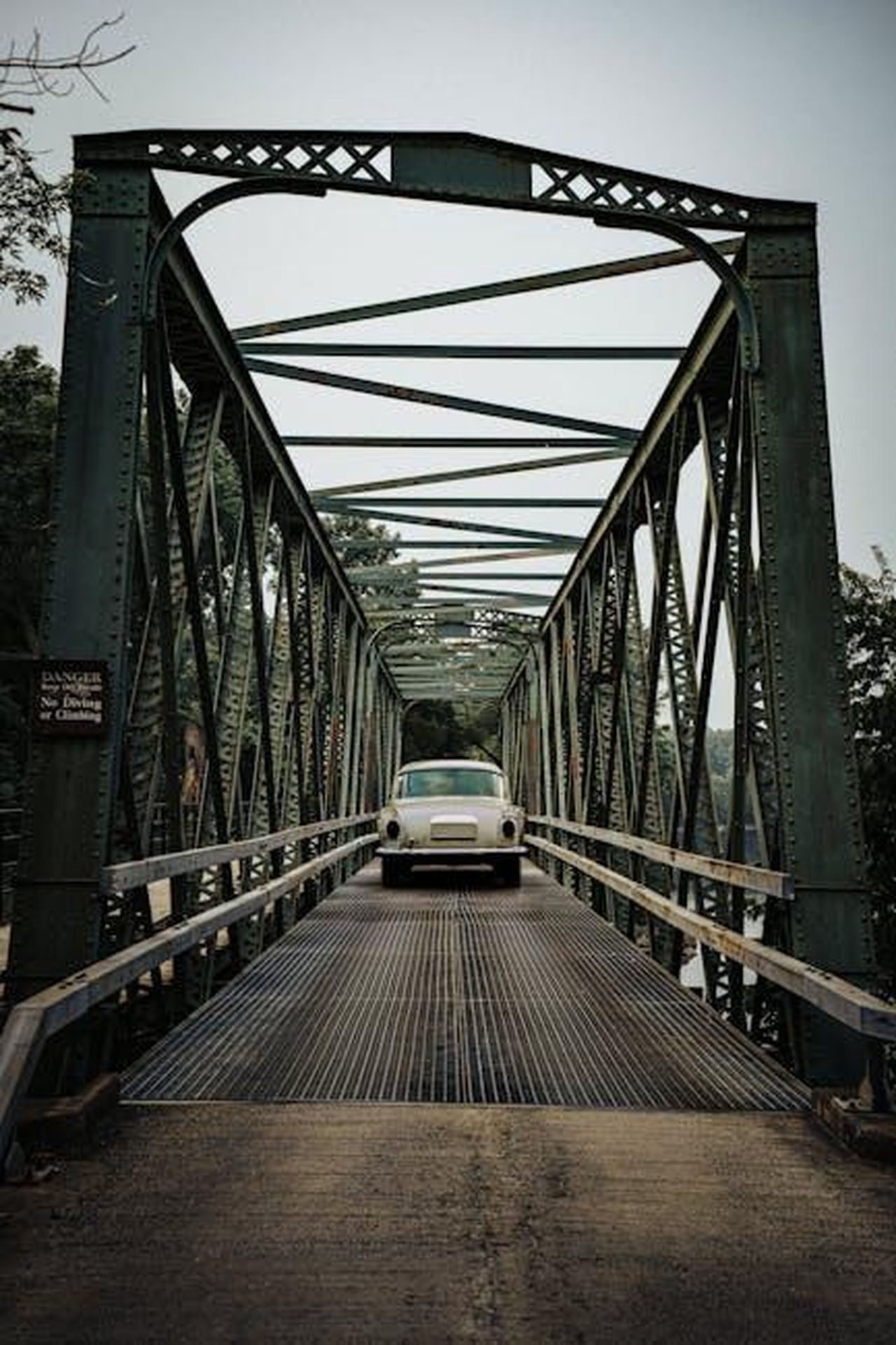 Dettagli_sullasta_e_sul_veicolo_I4itcLYjsG - Veicoli24 Source: Connor McManus - pexels - Classic vintage car crossing an old iron bridge surrounded by greenery.