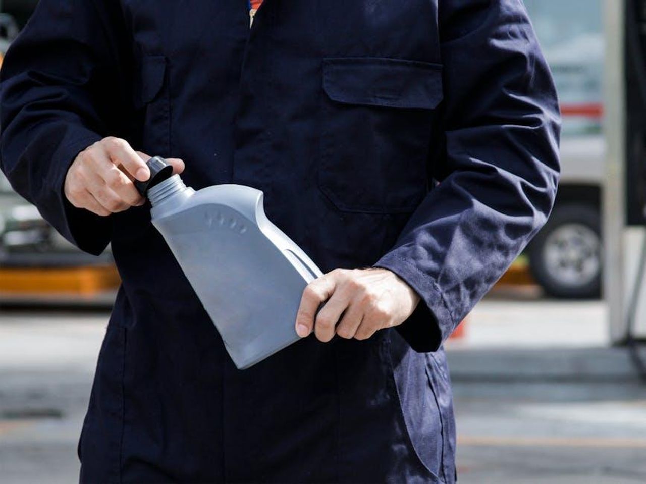 Download_disponibili_2200rNUZVo - Veicoli24 Source: Chrystian Guedez - pexels - Close-up of a mechanic in a blue uniform holding a gray oil container on a city street.