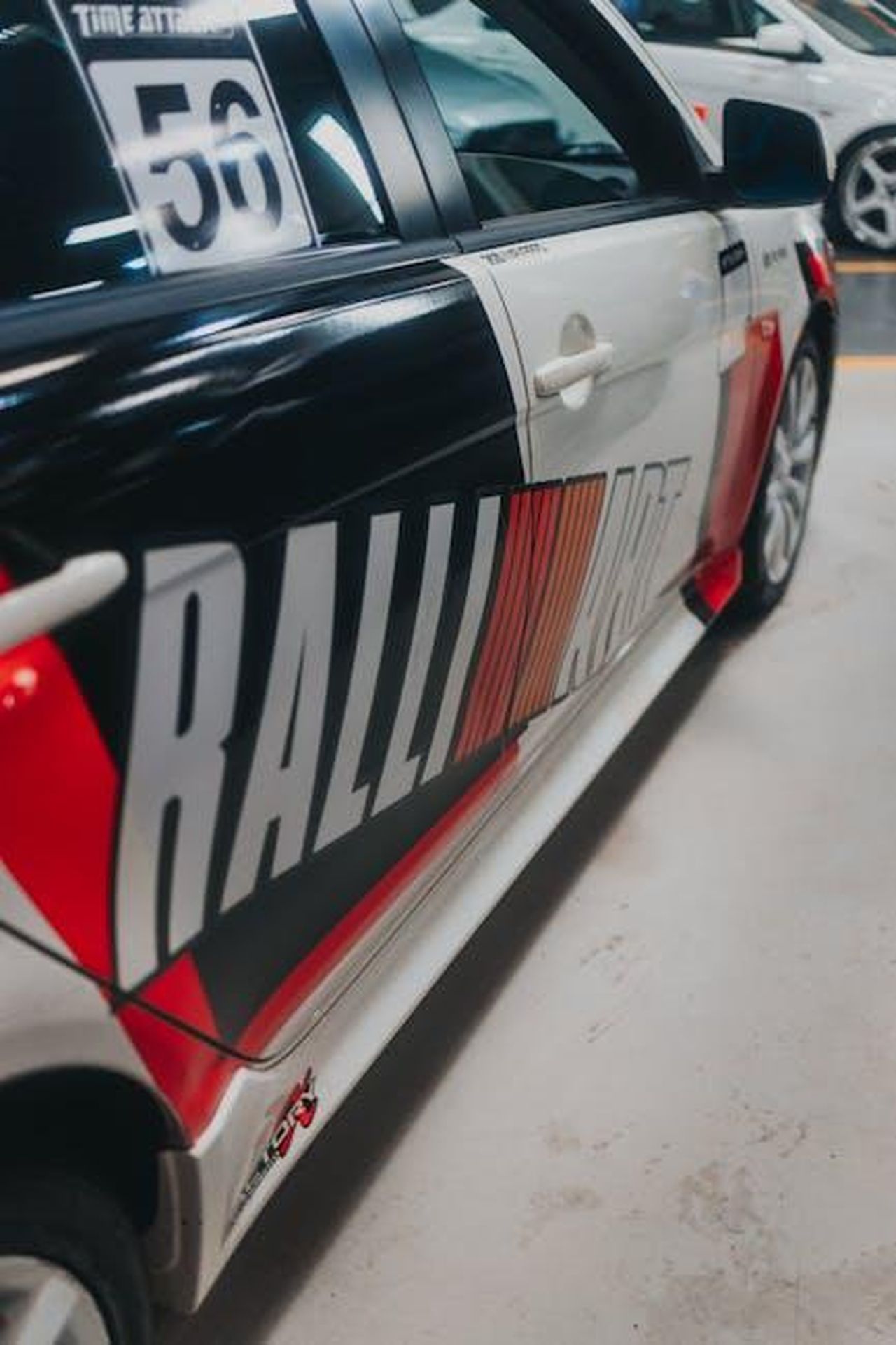 Futuro_del_Ralliart_e_altre_edizioni_0NvHMAQ1UR - Veicoli24 Source: Matheus Bertelli - pexels - Detailed side view of a Mitsubishi Ralliart car with livery design in an indoor parking area.