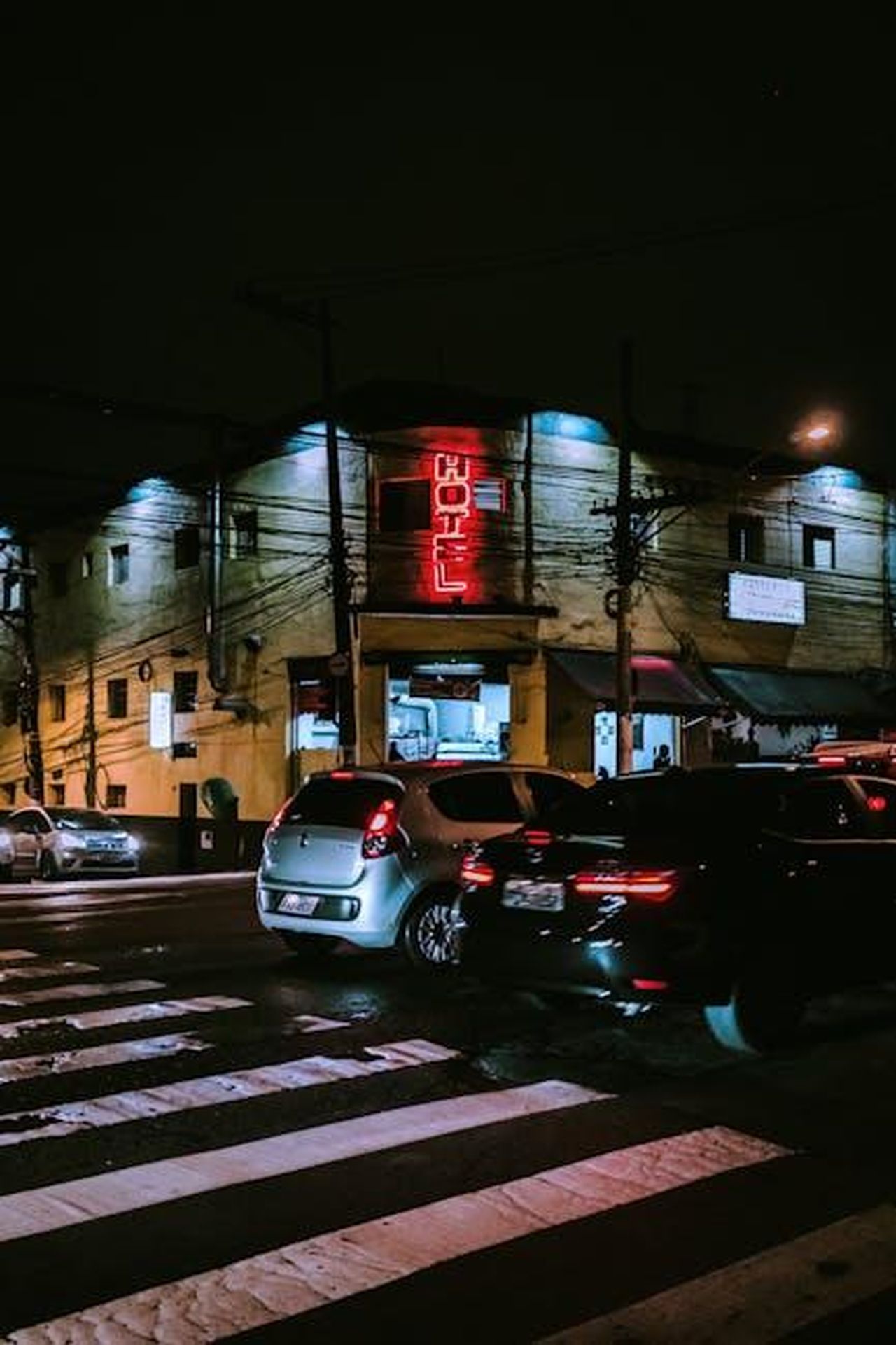Futuro_della_gamma_Volvo_fN7UqNoo0J - Veicoli24 Source: Thgusstavo Santana - pexels - Nighttime urban scene featuring cars at a crosswalk under neon signs and streetlights.