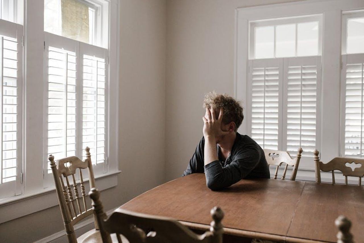 Gestire_il_carico_operativo_U9MfcXKOLl - Veicoli24 Source: Andrew Neel - pexels - A man sits alone at a table in a bright room, displaying deep contemplation.