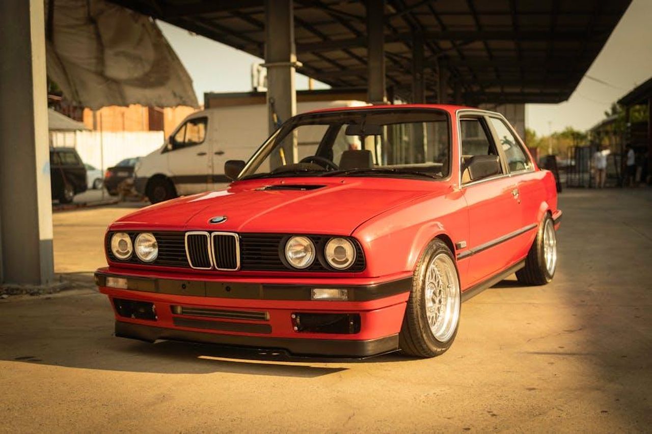 Il_confronto_tra_Toyota_Camry_e_Honda_Accord_nel_2025_HrptX3A3gq - Veicoli24 Source: Nate Biddle - pexels - A classic red BMW E30 coupe parked in an industrial setting under warm sunlight.