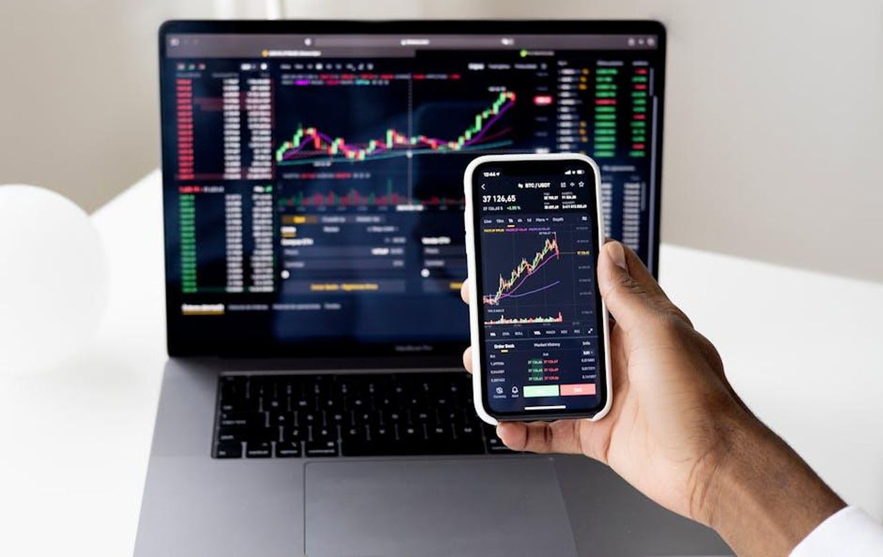 Il_crollo_del_valore_di_Nikola_da_30_miliardi_a_74_milioni_JaSIlSw1Z9 - Veicoli24 Source: Anna Nekrashevich - pexels - Person checking stock market graphs on laptop and smartphone, focusing on financial data.