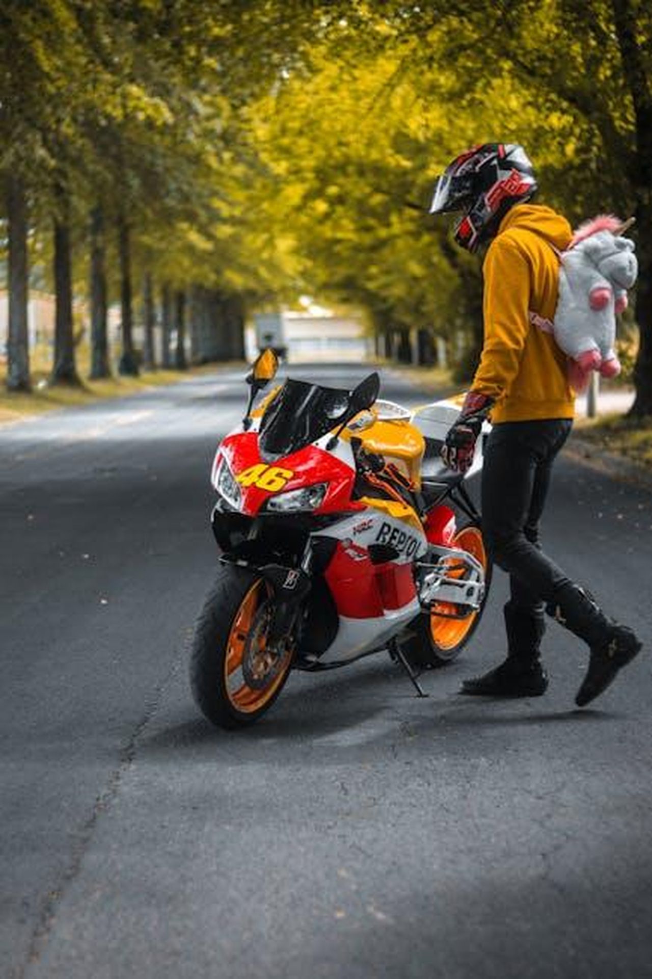 Il_numero_46_simbolo_di_un_pilota_eccezionale_Ldv2ltrSko - Veicoli24 Source: Louis_ftn_ - pexels - Man with toy backpack standing by Honda motorcycle on a tree-lined road.