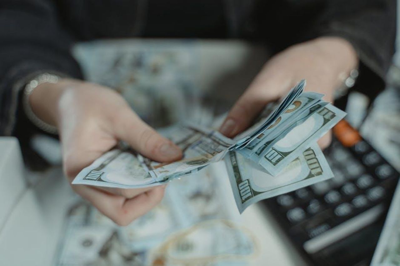 Il_ruolo_di_Axel_Dewitz_e_il_suo_predecessore_RhEWFH0NUf - Veicoli24 Source: Tima Miroshnichenko - pexels - Close-up of hands counting hundred dollar bills with a calculator in the background.