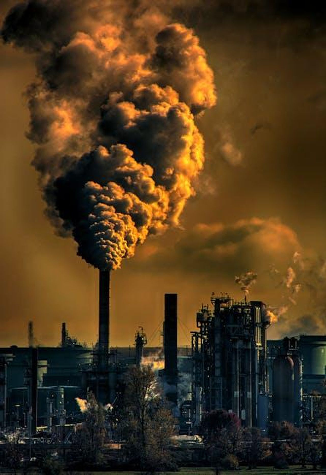 Impatto_delle_normative_sulle_emissioni_e_delle_politiche_di_prezzo_TaPEI36hO7 - Veicoli24 Source: Chris LeBoutillier - pexels - A factory emitting smoke clouds against a dark sunset sky, illustrating air pollution and industrial impact.