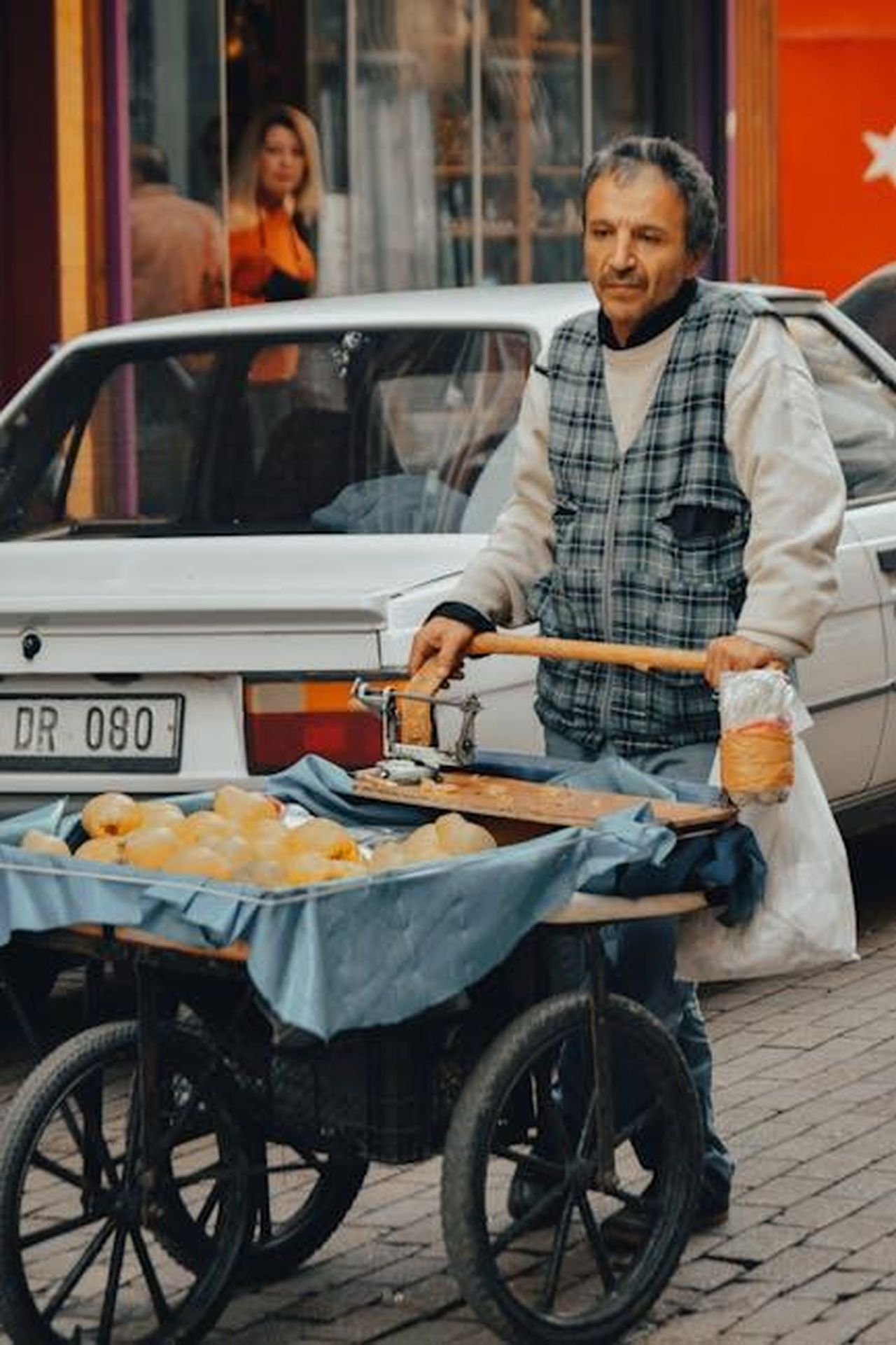 Impatto_delle_politiche_sulloccupazione_nel_settore_automobilistico_HdKuKWIOrk - Veicoli24 Source: withatices - pexels - Man in plaid vest pushing a food cart on a bustling street.