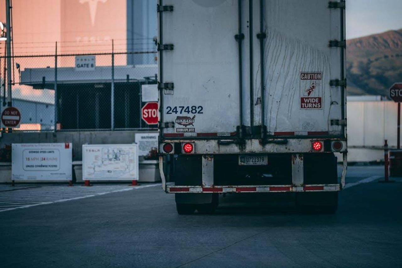 Indagine_di_Tesla_su_richiesta_di_unagenzia_di_regolamentazione_non_statunitense_ar9NIpTMls - Veicoli24 Source: Craig Adderley - pexels - Semi truck parked at a loading dock with visible caution signs and industrial surroundings.