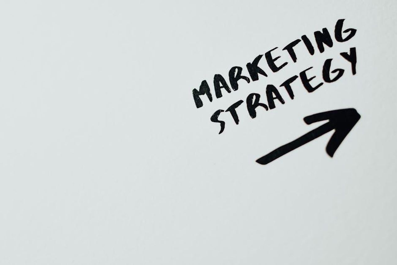 Iniziative_di_marketing_congiunto_8yF2yfnYvj - Veicoli24 Source: Eva Bronzini - pexels - Close-up of handwritten 'Marketing Strategy' text with an arrow on white background.