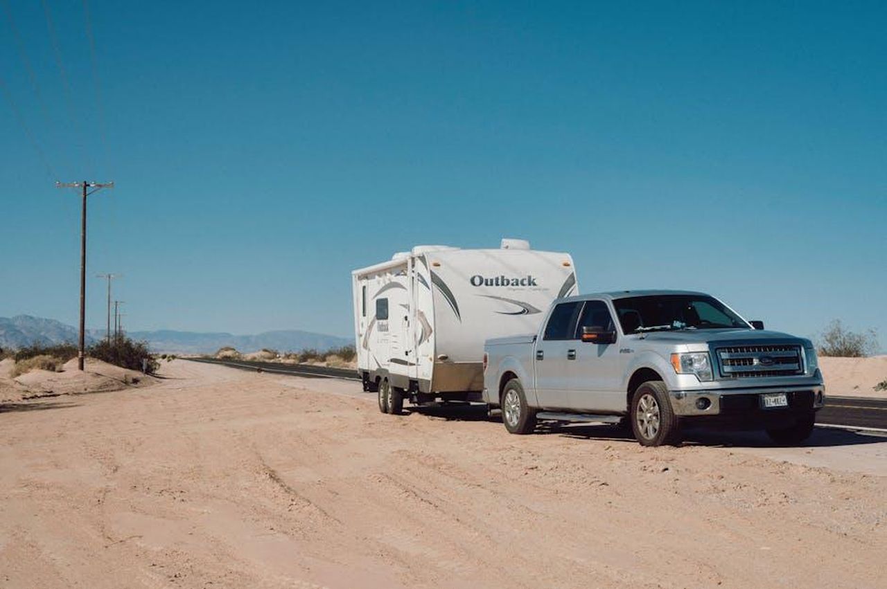Innovazioni_di_Ford_nel_traino_di_veicoli_elettrici_jmwNc5uq2A - Veicoli24 Source: Alfo Medeiros - pexels - Silver truck towing an Outback trailer on a desert road under clear blue skies.