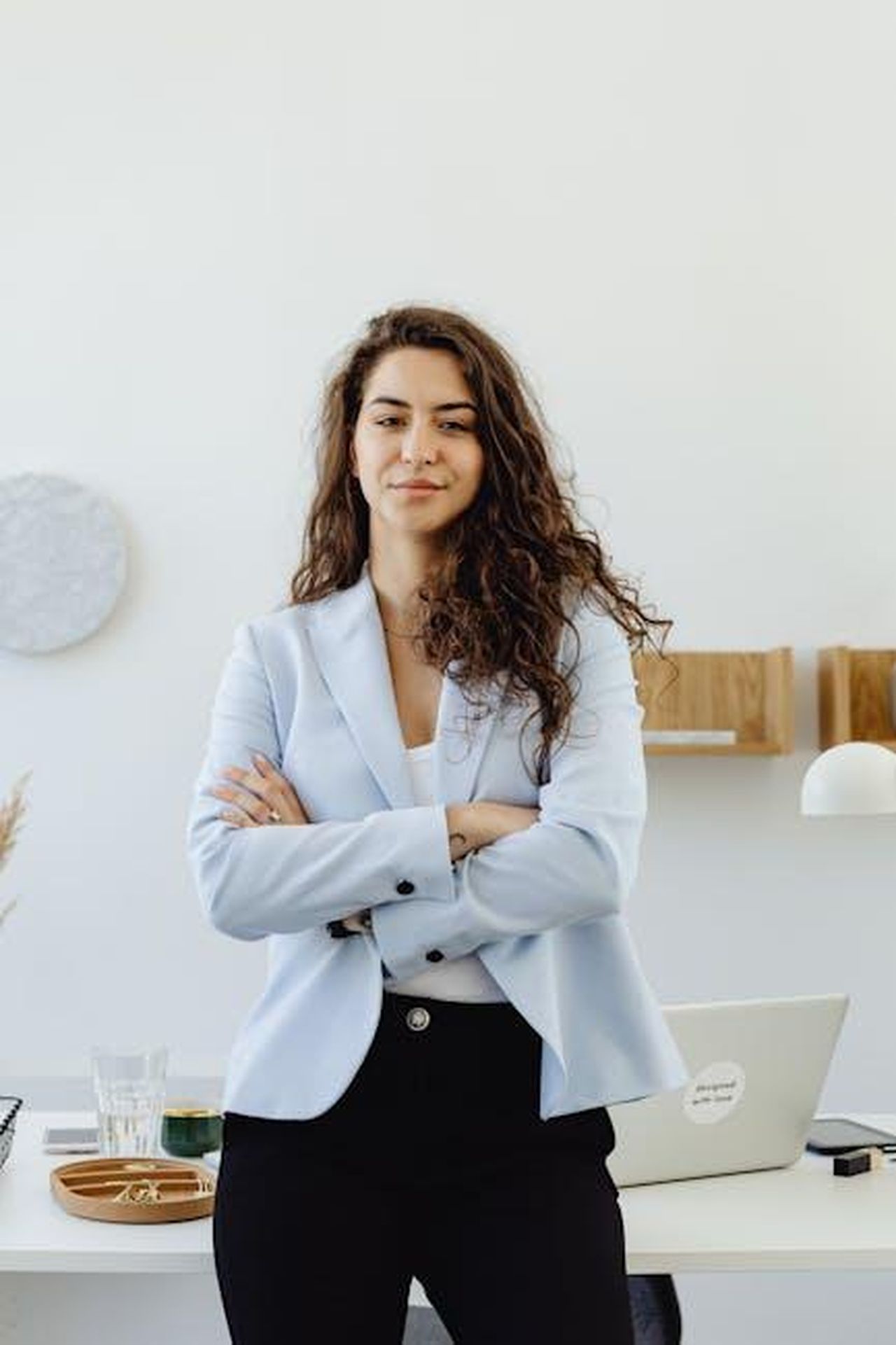 La_carriera_di_Peter_Rawlinson_iZJmqRrjpA - Veicoli24 Source: Photo By: Kaboompics.com - pexels - Professional woman in a white blazer standing confidently in an office with arms crossed.