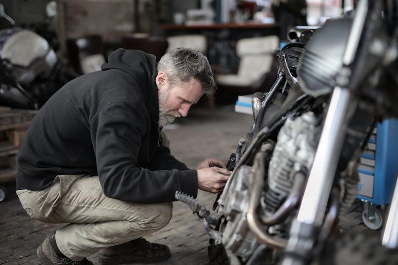 La_resistenza_al_cambiamento_nellindustria_automobilistica_QPBXE5M1Bf - Veicoli24 Source: Andrea Piacquadio - pexels - Side view of focused male mechanic in casual wear sitting near motorbike and examining details details in workshop
