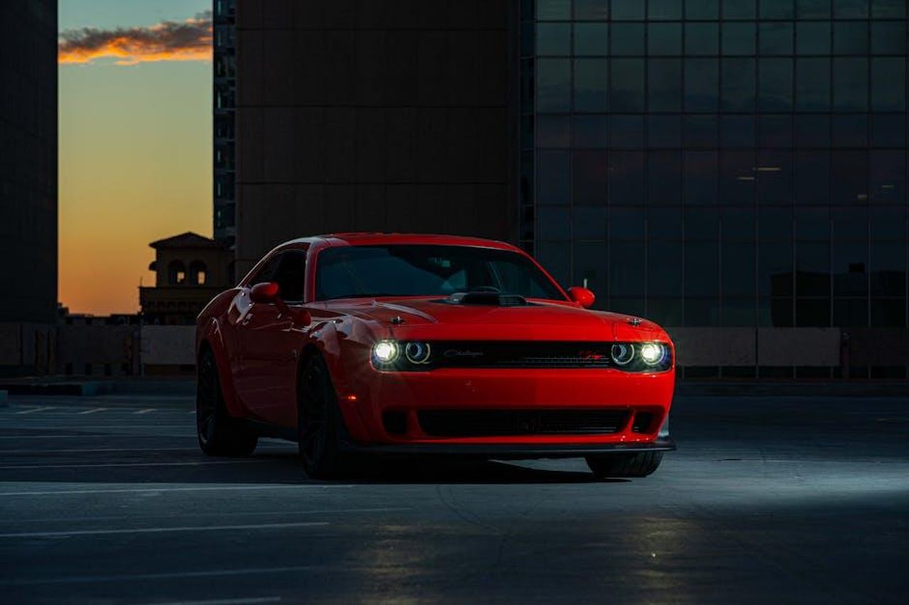 La_visione_di_Matt_McAlear_per_Dodge_0Bjzm3qJOD - Veicoli24 Source: Derwin Edwards - pexels - A striking red Dodge Challenger parked outdoors in an urban area at twilight.