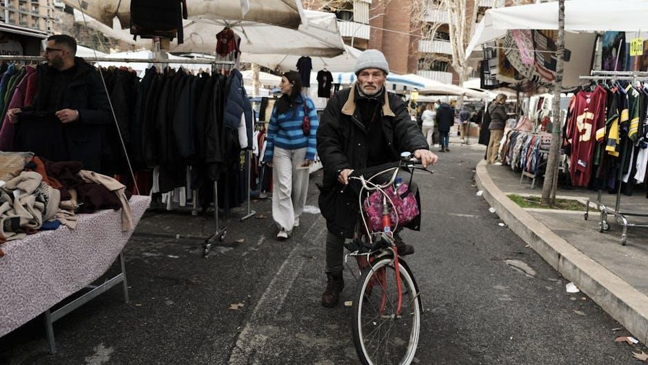 Le_performance_dei_PHEV_nel_2024_Zm6MKP07XA - Veicoli24 Source: Can İğdeli - pexels - A man rides a bicycle through a bustling outdoor market filled with clothing stalls.