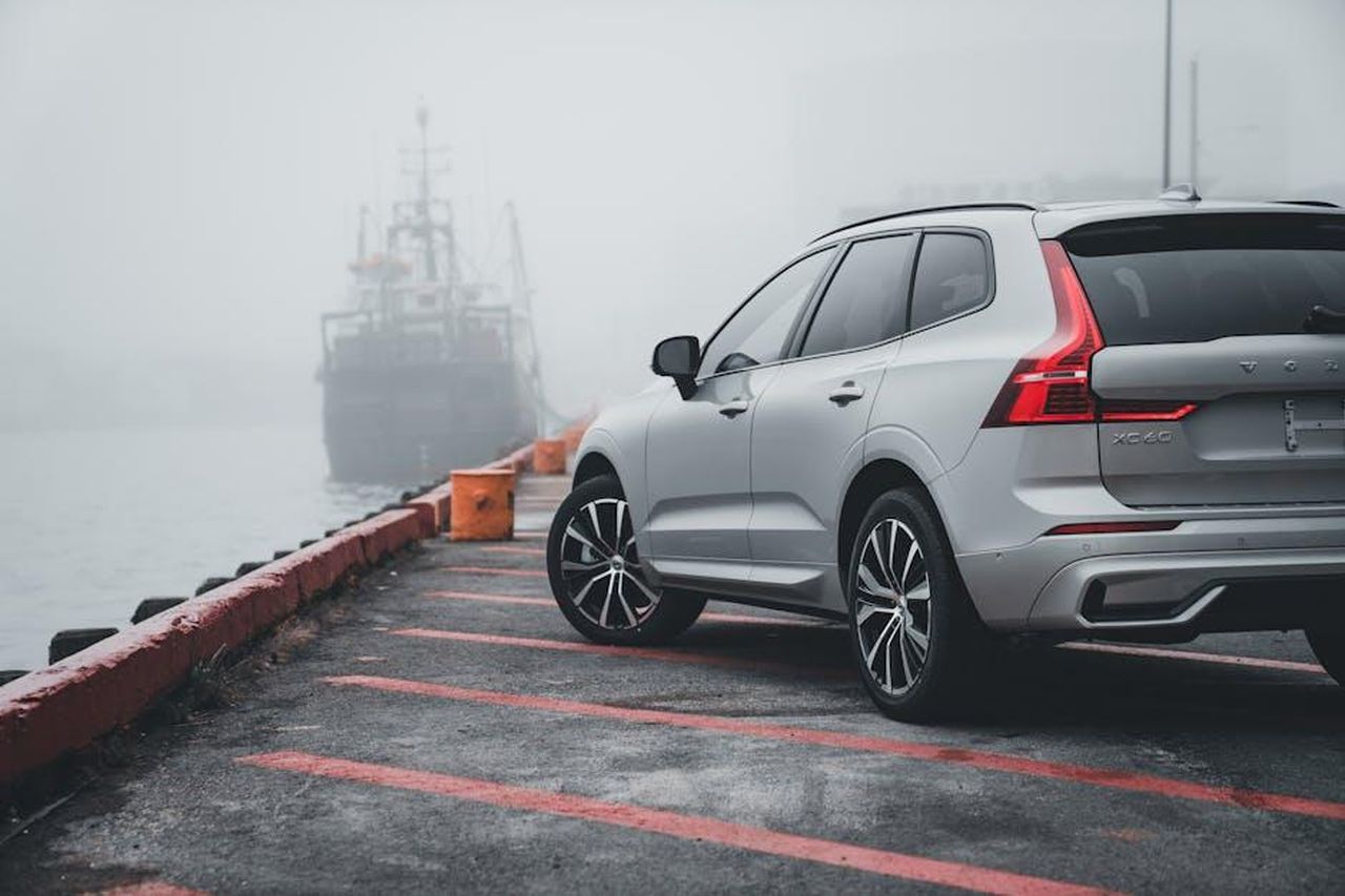Motorizzazioni_e_modelli_futuri_RtNTsZRIzl - Veicoli24 Source: Erik Mclean - pexels - A sleek Volvo XC60 parked by a foggy harbor, with a ship in the background, creating a mysterious and serene atmosphere.