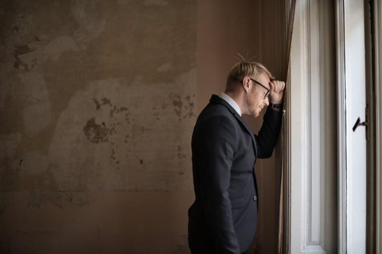 Nissan_cerca_investitori_la_situazione_finanziaria__critica_xkuBDM0sIy - Veicoli24 Source: Andrea Piacquadio - pexels - A worried businessman in a suit leaning against a window, expressing stress and concern.