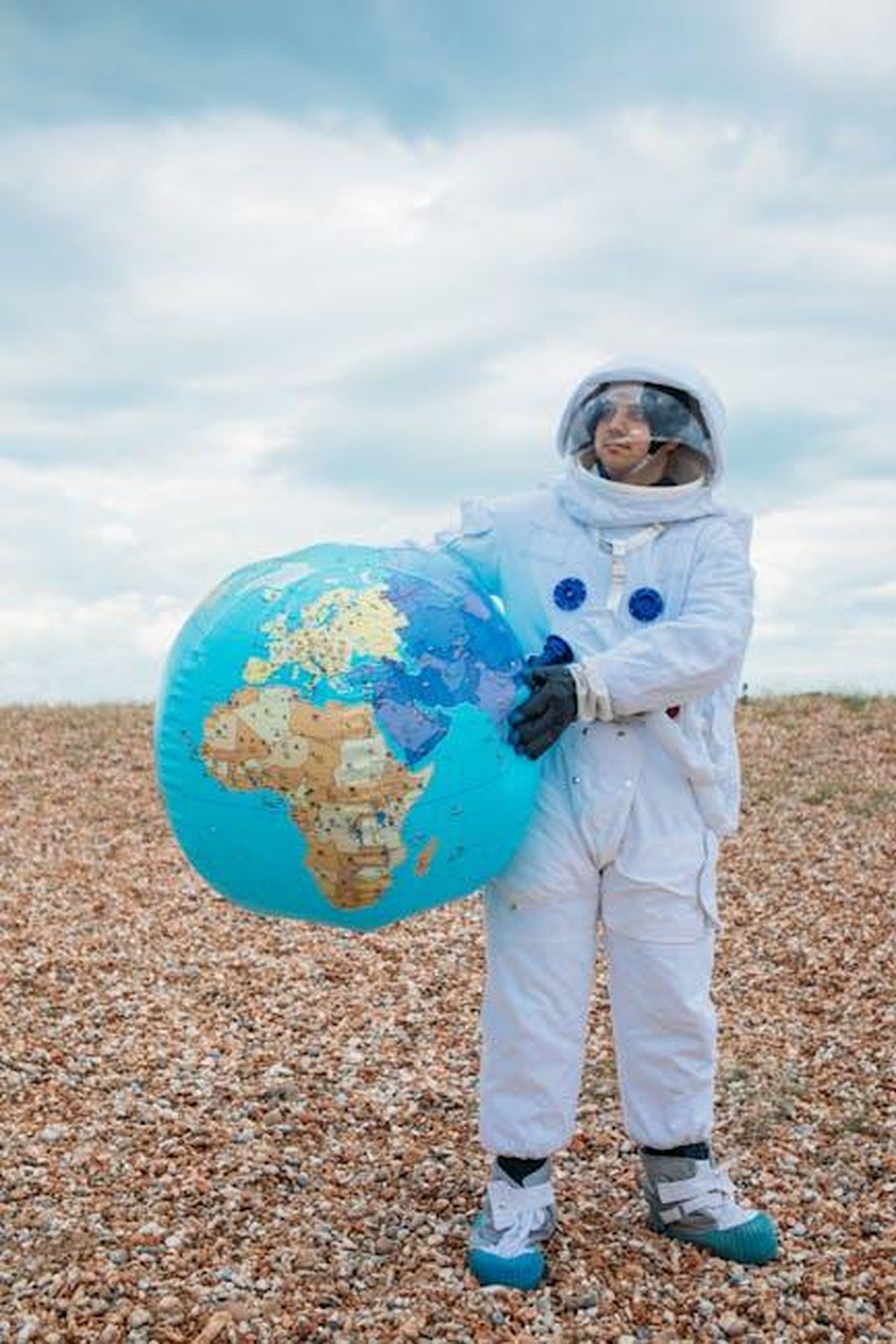 Nomina_di_Chris_Yang_a_ruoli_globali_oN8glrxmRs - Veicoli24 Source: T Leish - pexels - A person in an astronaut costume holding an inflatable globe standing on a rocky terrain under a cloudy sky.