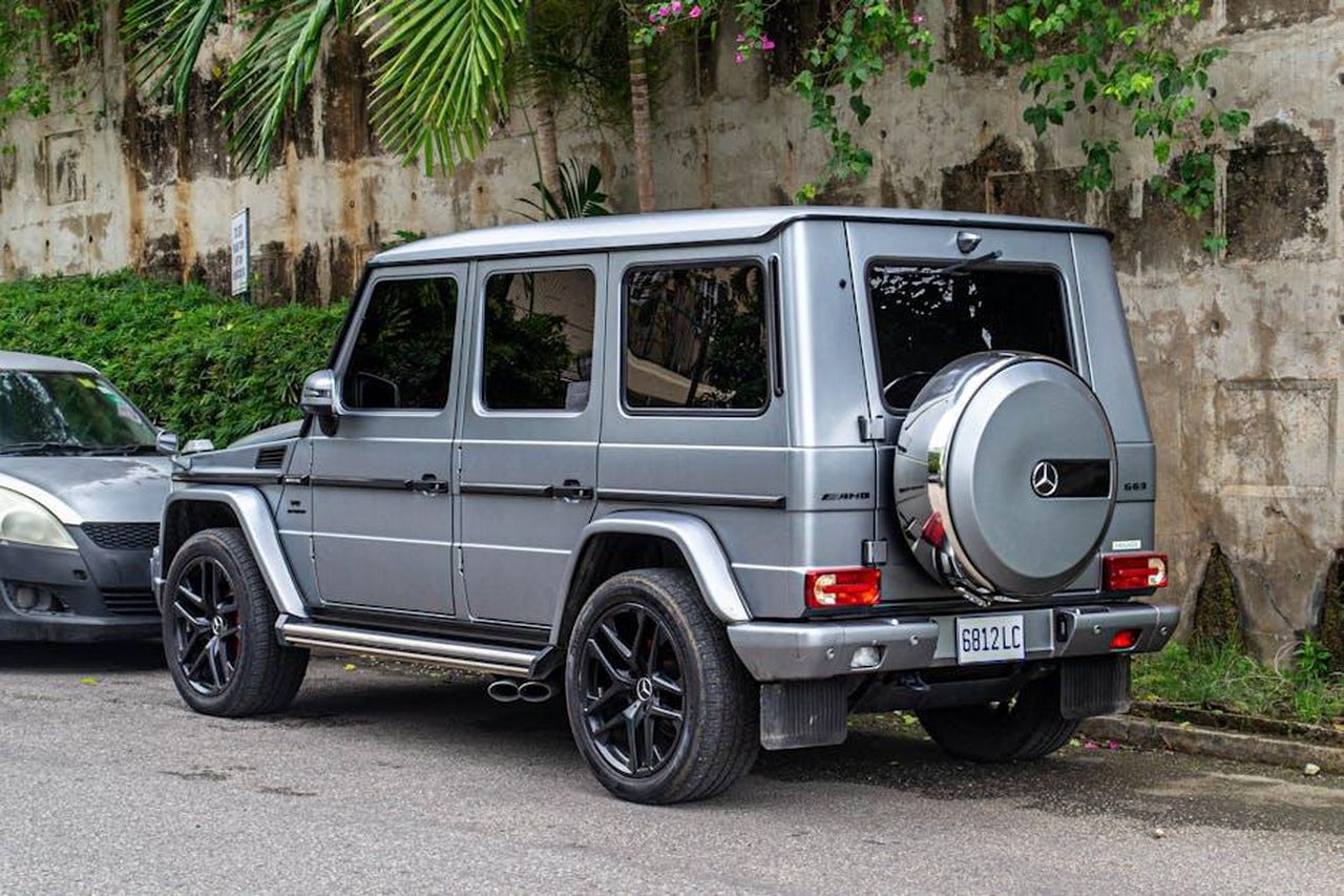 Novit_per_la_GClass_2024_buKstEamJn - Veicoli24 Source: hh meddia_ - pexels - Silver luxury SUV with custom rims parked outdoors in scenic Jamaican street with lush green foliage.