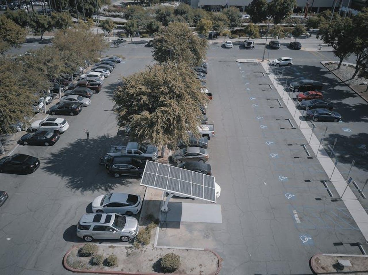 Nuovi_modelli_di_veicoli_elettrici_in_arrivo_TOAxx1TmVN - Veicoli24 Source: Kindel Media - pexels - Aerial view of a solar panel charging station in a busy parking lot surrounded by cars and trees.