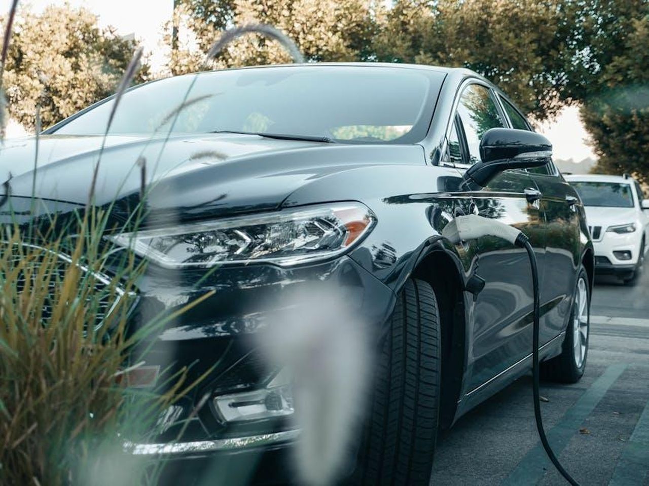 Performance_dei_veicoli_ibridi_e_plugin_8dALaTAB1i - Veicoli24 Source: Kindel Media - pexels - A black hybrid car charging at an outdoor station surrounded by greenery.