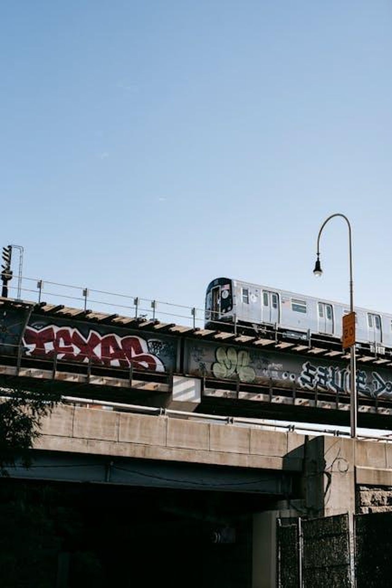 Piattaforma_EGMP_e_opzioni_di_batteria_sD7DfDiwgF - Veicoli24 Source: Charles Parker - pexels - Urban train crossing a graffiti-covered bridge under clear blue sky, depicting vibrant city life.