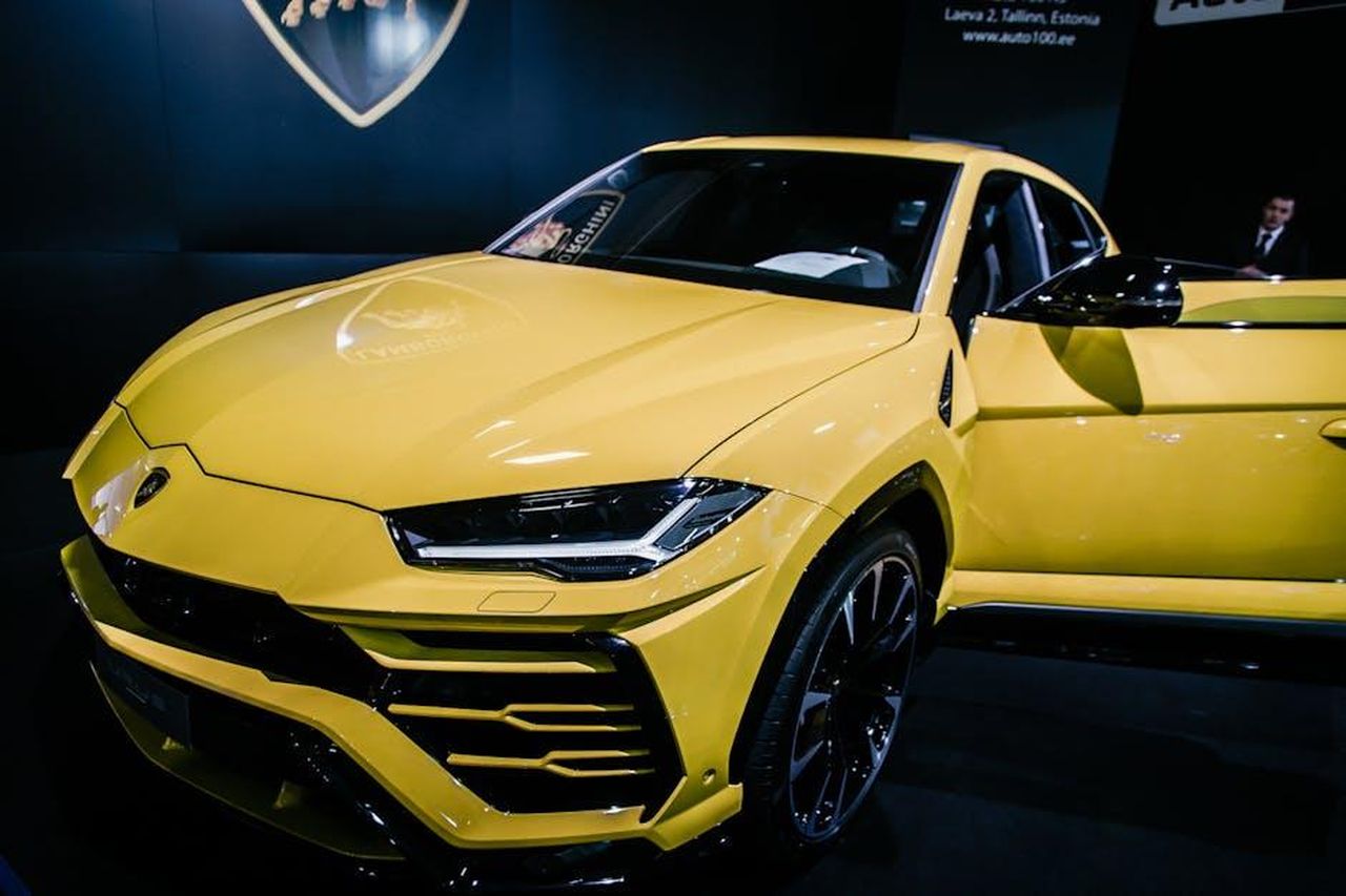 Possibile_nome_e_design_del_SUV_njxhXvmsl1 - Veicoli24 Source: Toms Svilans - pexels - A stunning yellow luxury SUV on display at an auto show under bright lights.