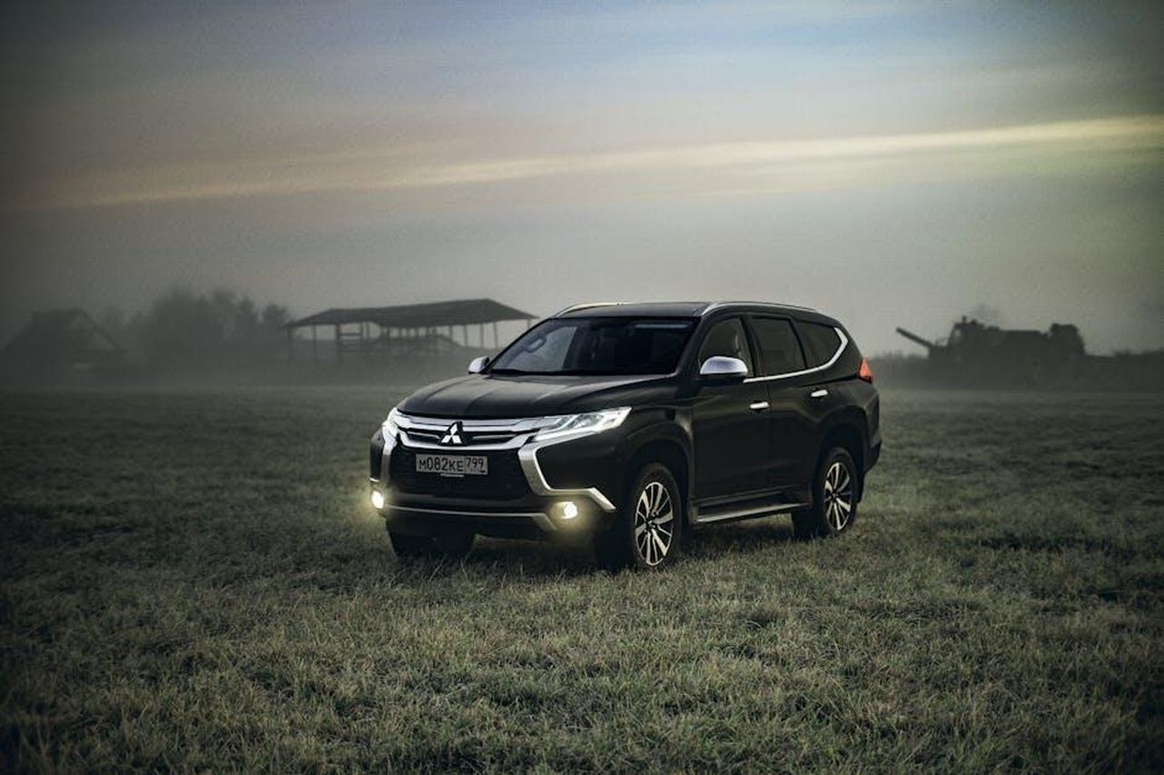 Prestazioni_della_Mitsubishi_Outlander_2025_lKFBVeNJKG - Veicoli24 Source: S. von Hoerst - pexels - A black Mitsubishi SUV stationed in a misty field during twilight, headlights on.